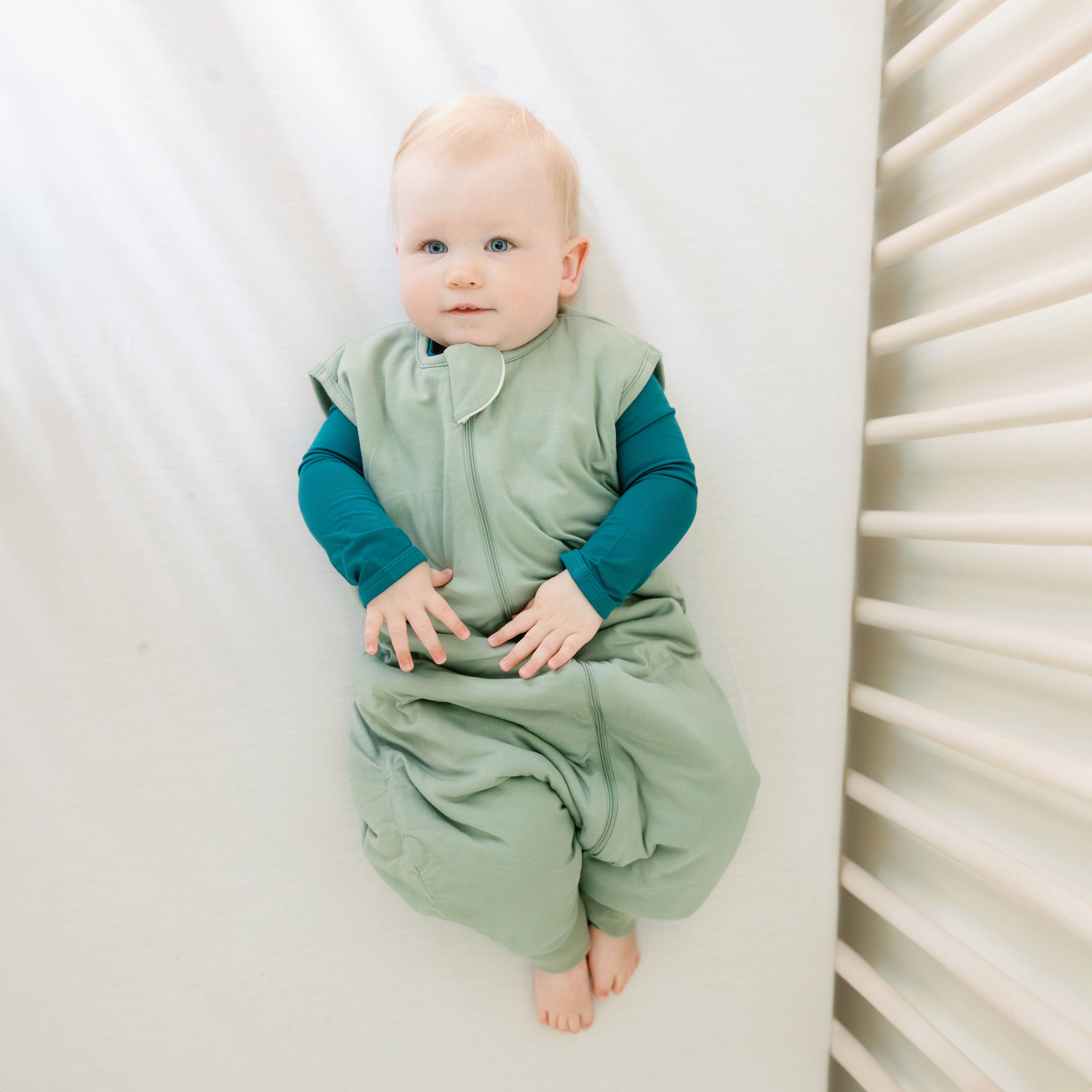 Infant model laying in a crib wearing the Sleep Bag Walker in Thyme 1.0