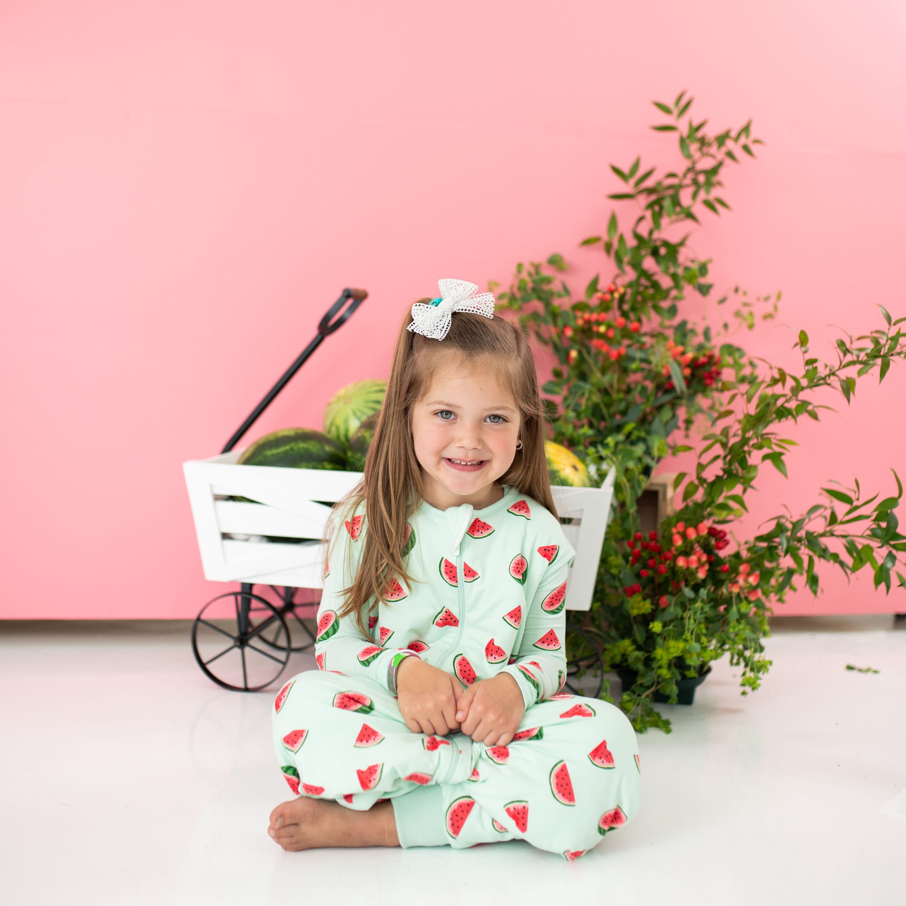 Young girl sitting cross legged on the floor wearing the Sleep Bag Walker in Watermelon 1.0 with matching long sleeve pajamas