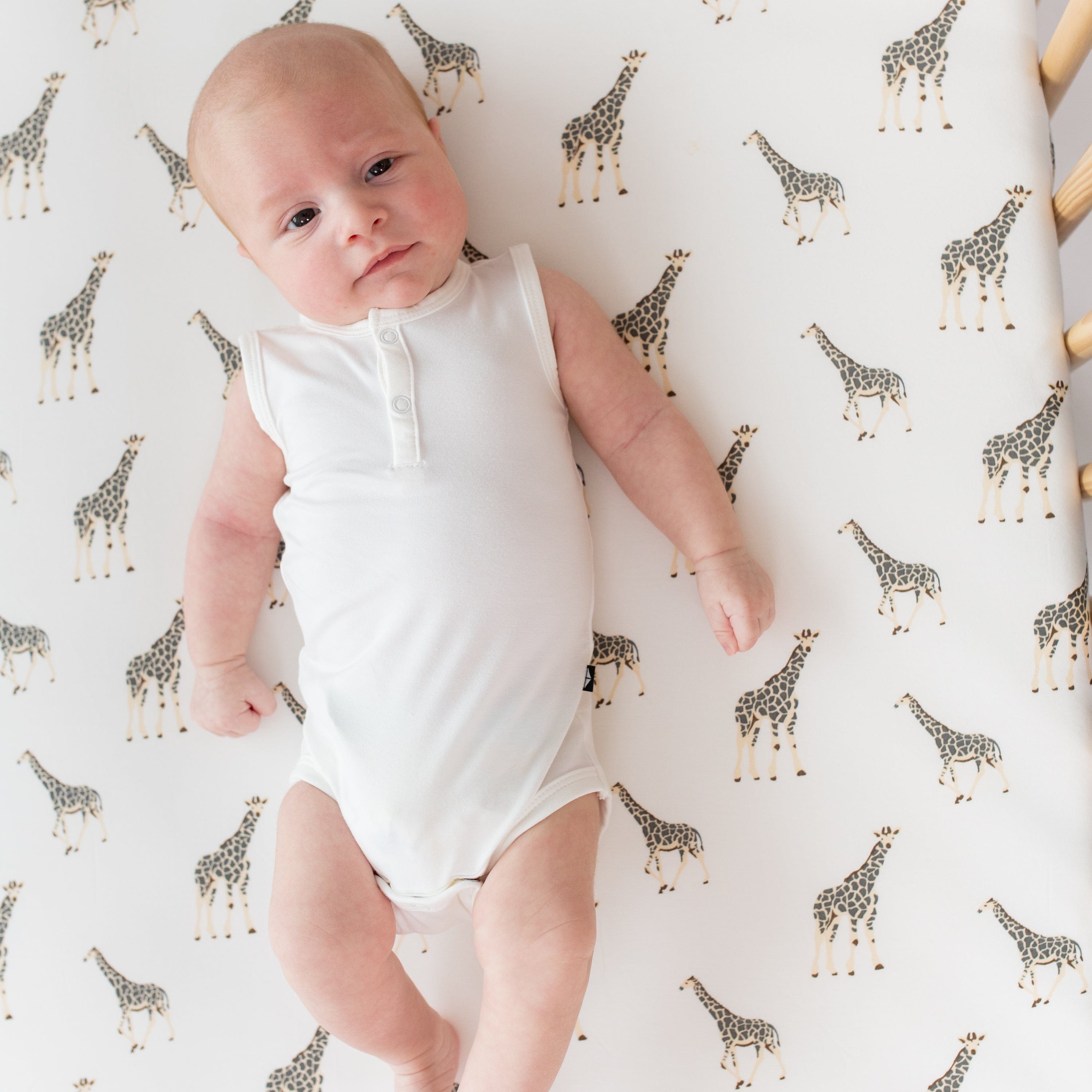 Infant laying on a crib sheet in Giraffe and wearing Kyte Baby Sleeveless Bodysuit in Cloud