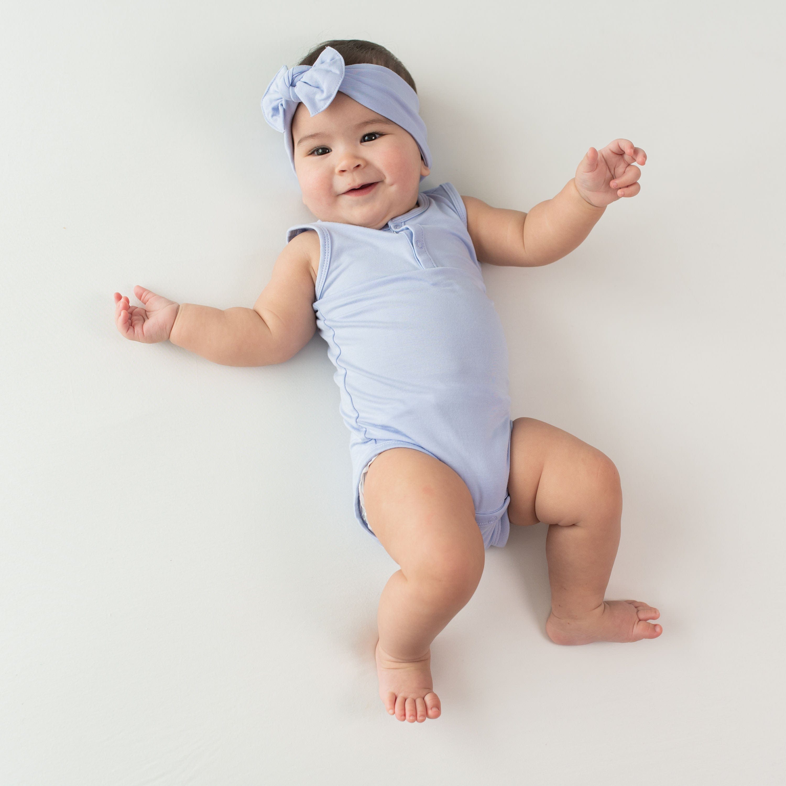 Infant wearing Kyte Baby henley style Sleeveless Bodysuit in Lilac purple with matching headband