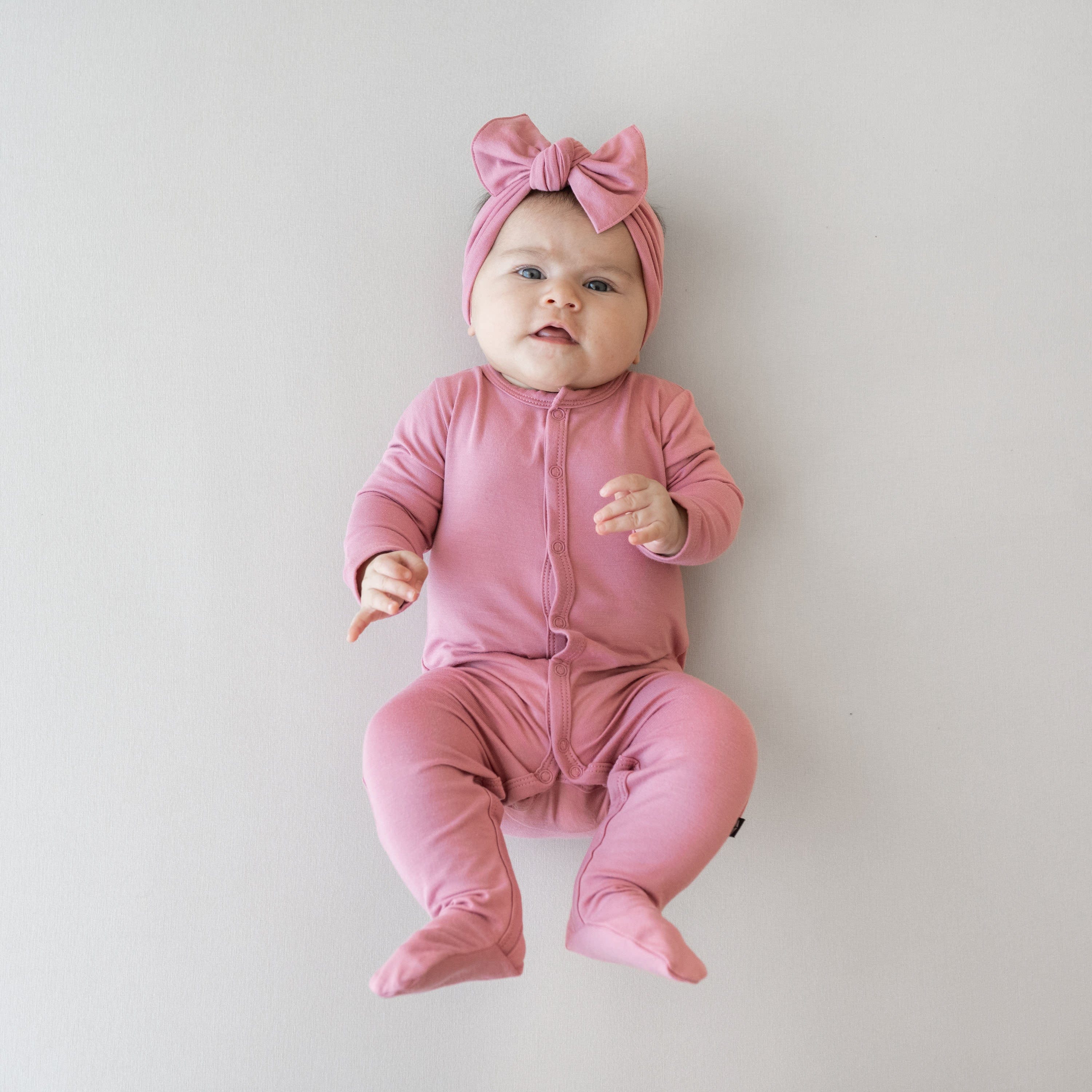 Baby wearing pink snap footie pajamas with matching bow headband