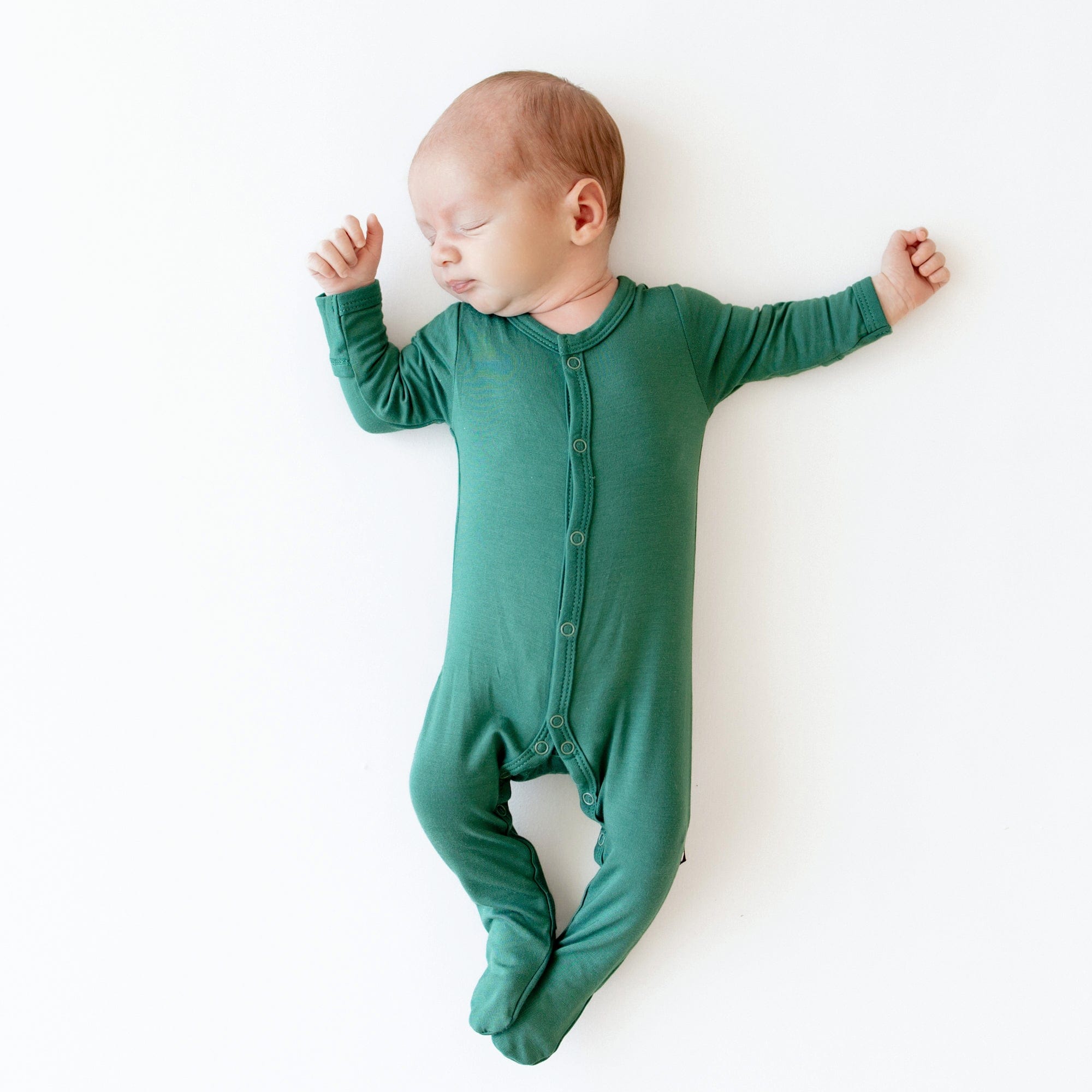 Sleeping newborn wearing Kyte Baby Footie in Emerald