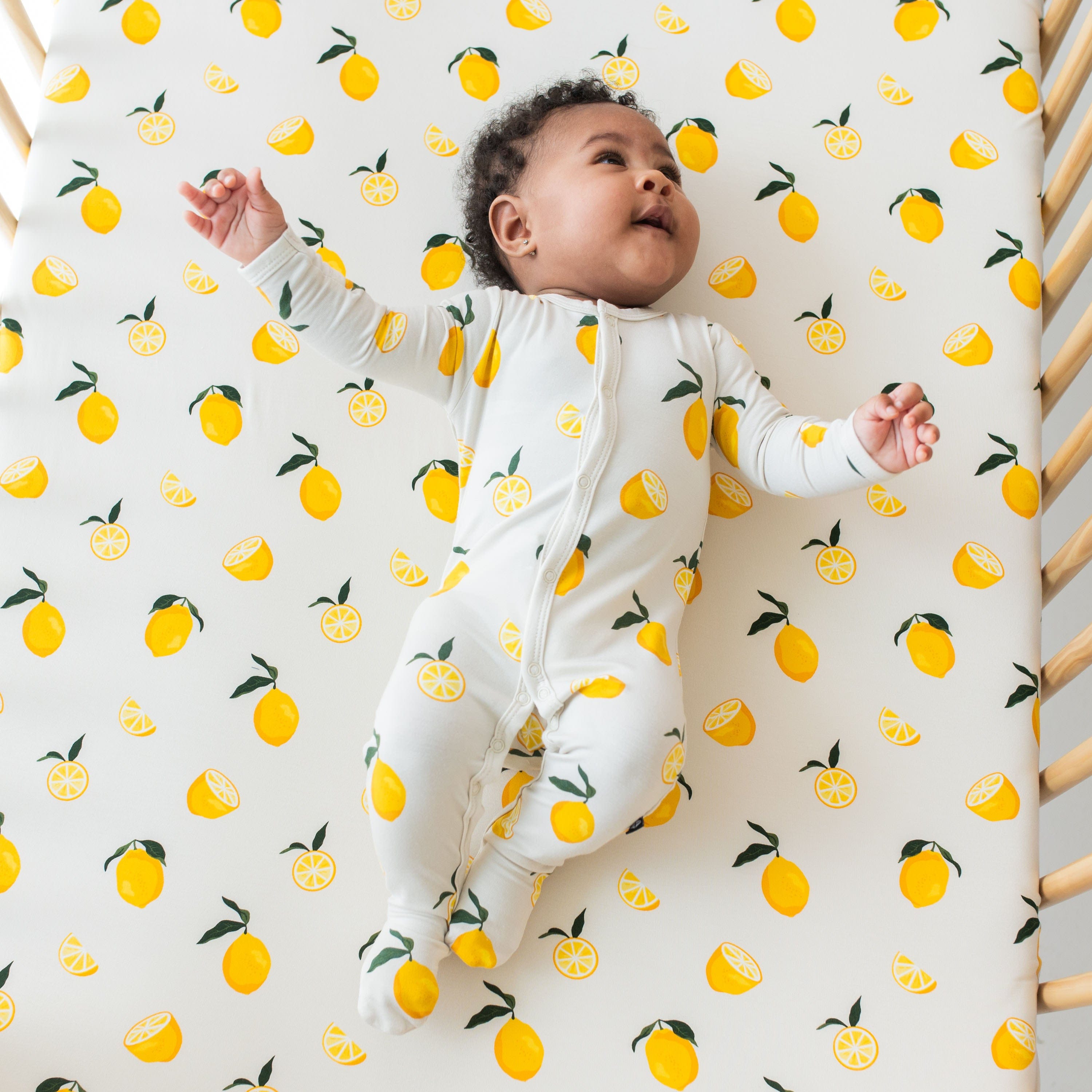 Baby wearing Lemon Snap Footie pajamas on matching crib sheet