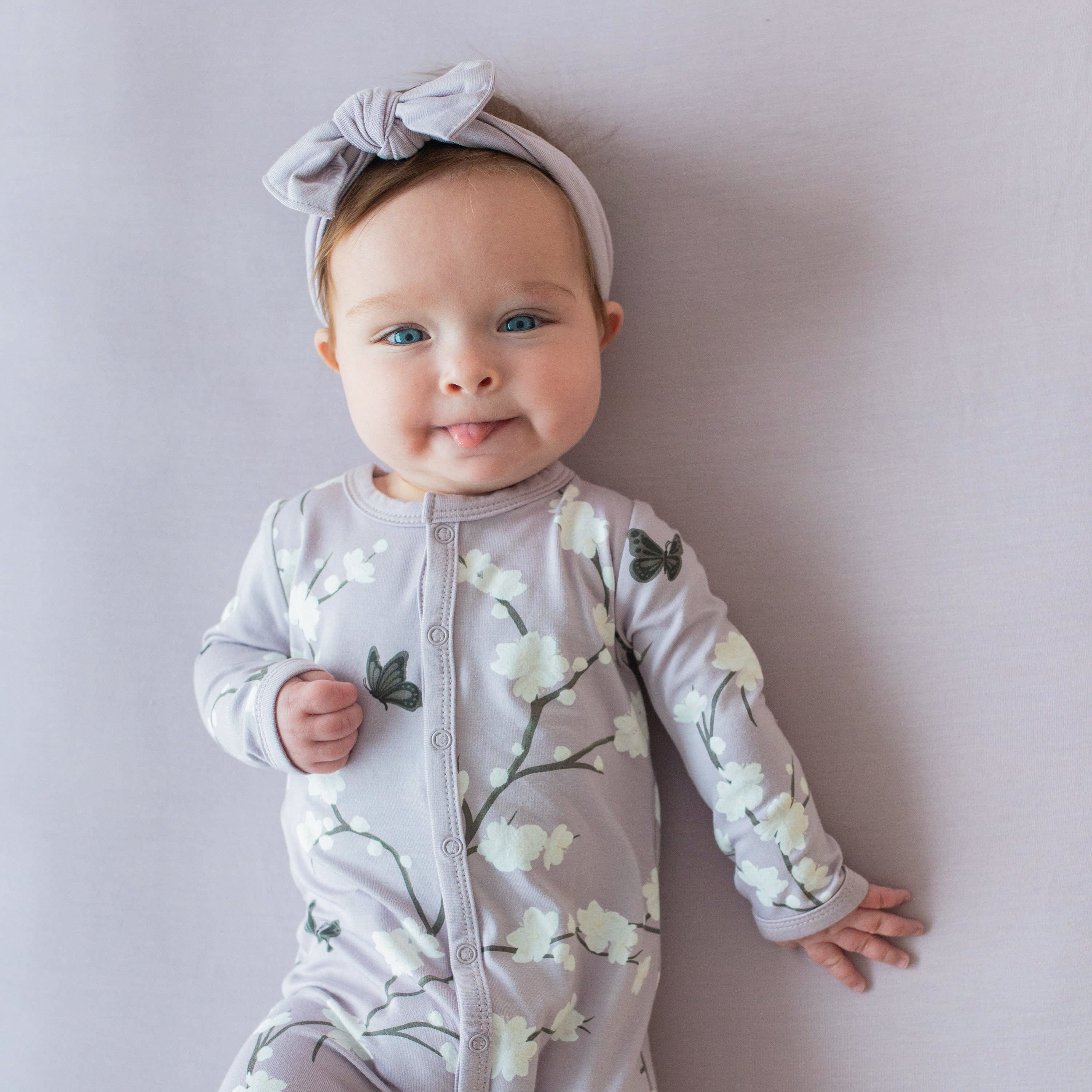 Child wearing long sleeve Kyte Baby Romper with snaps in Cherry Blossom with bow headband