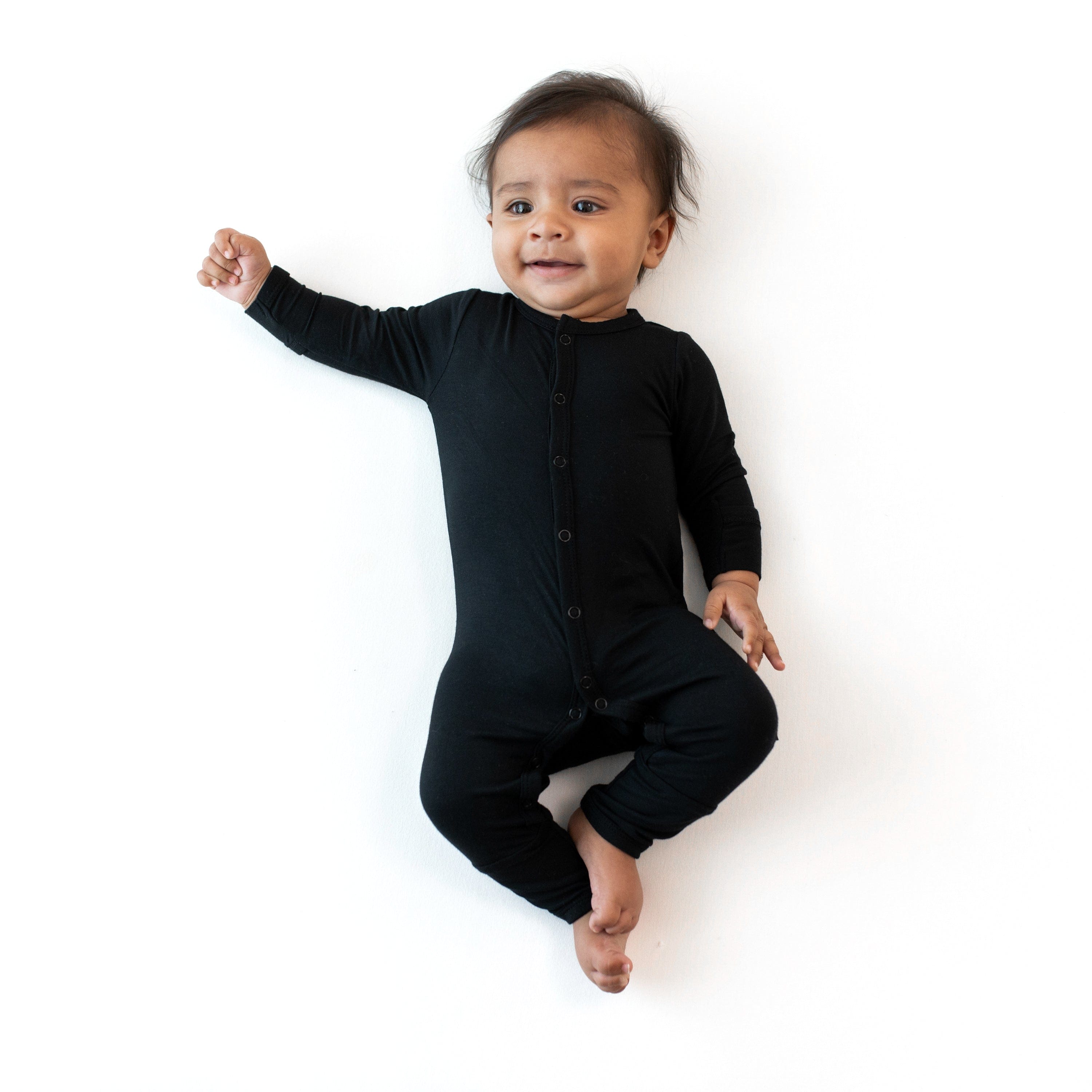 Baby laying on white surface wearing Kyte Baby Romper in Midnight