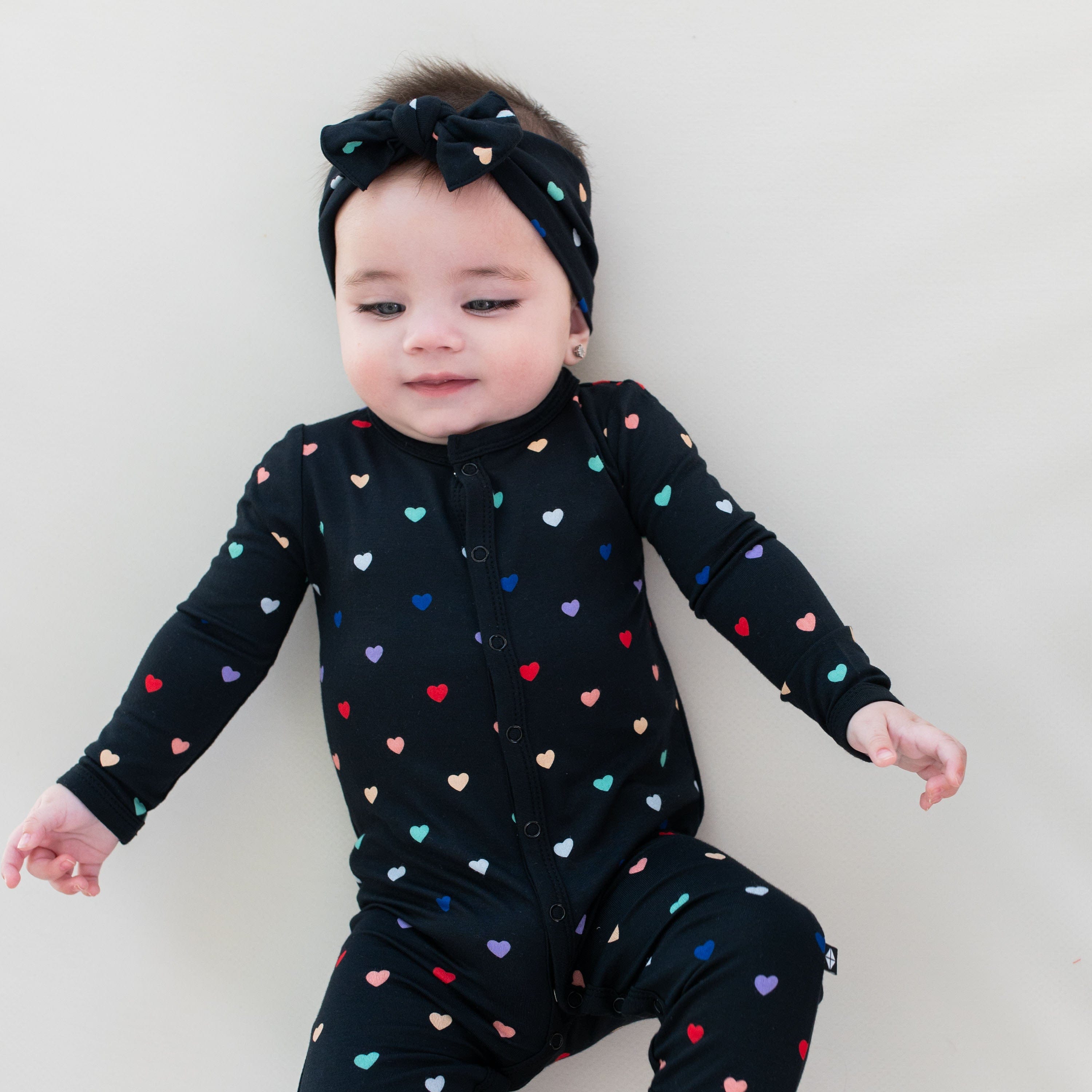 Child wearing long sleeve Kyte Baby Romper with snaps in Midnight Rainbow Heart