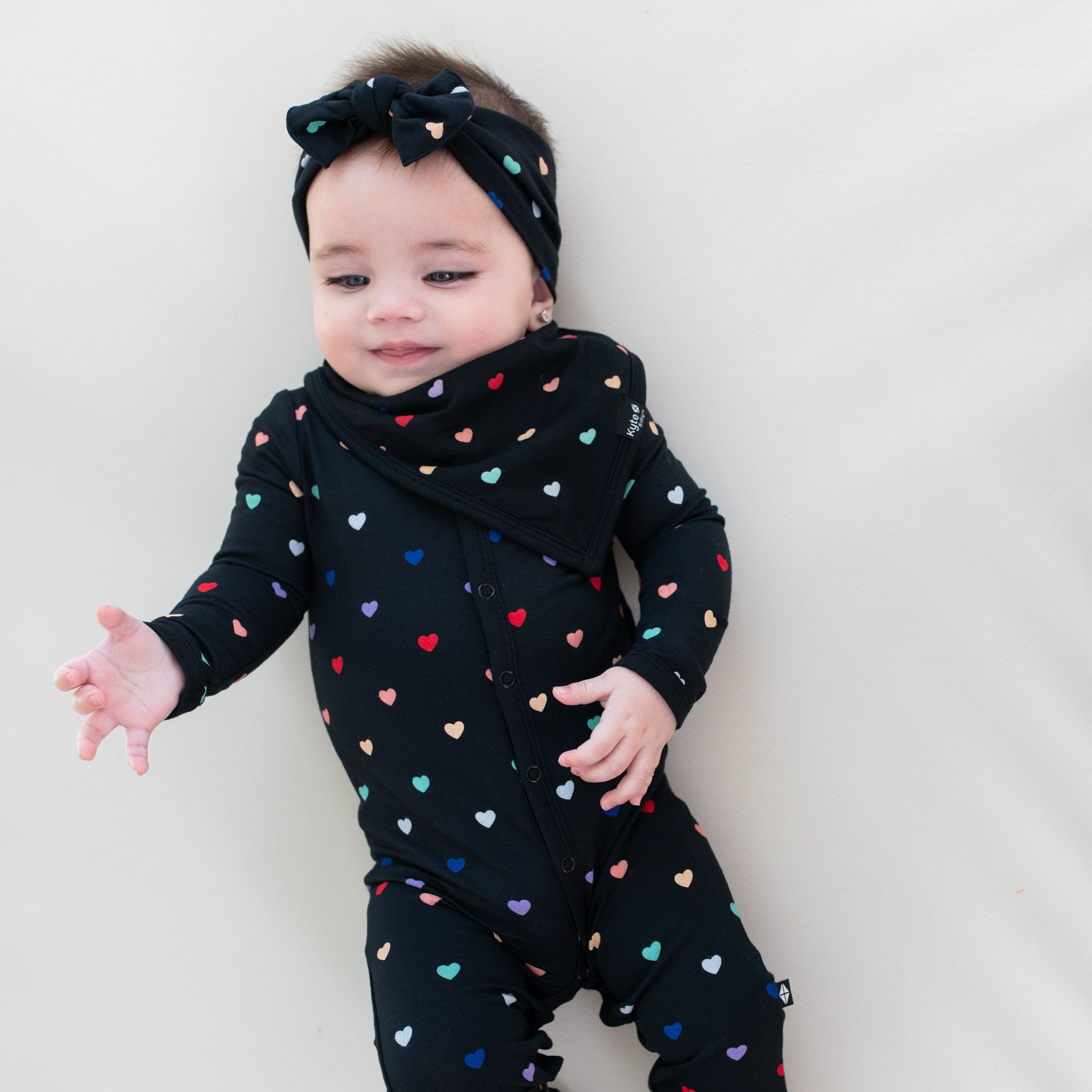 Infant wearing Kyte Baby Romper pajamas in Midnight Rainbow Heart