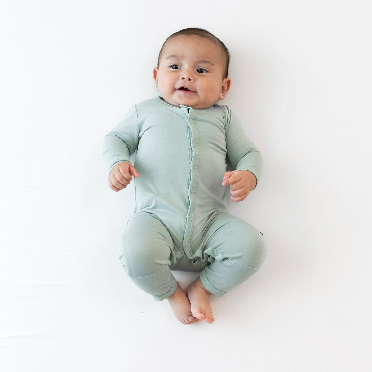 Baby laying on white surface while wearing Kyte Baby Romper in Sage