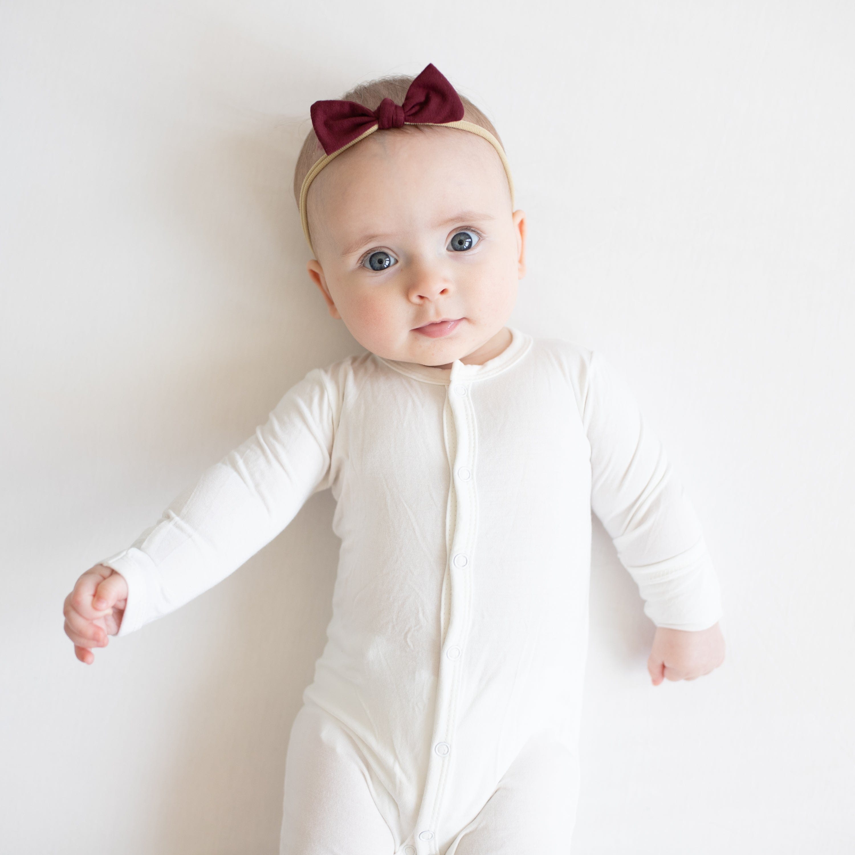 Infant wearing Kyte Baby Tiny Bow with Nylon Band in Burgundy