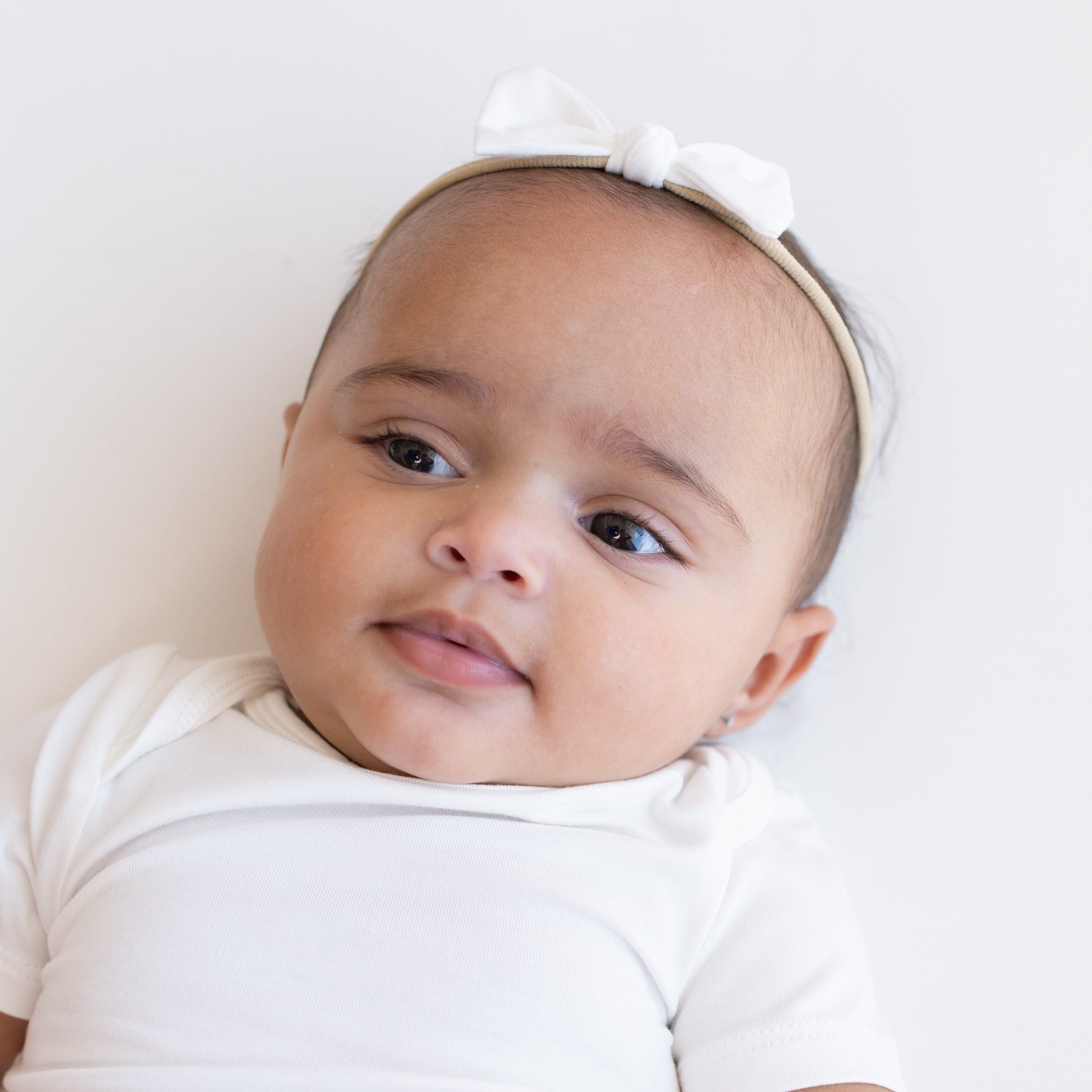 Infant laying on white background while wearing Kyte Baby Tiny Bow with Nylon Band in Cloud