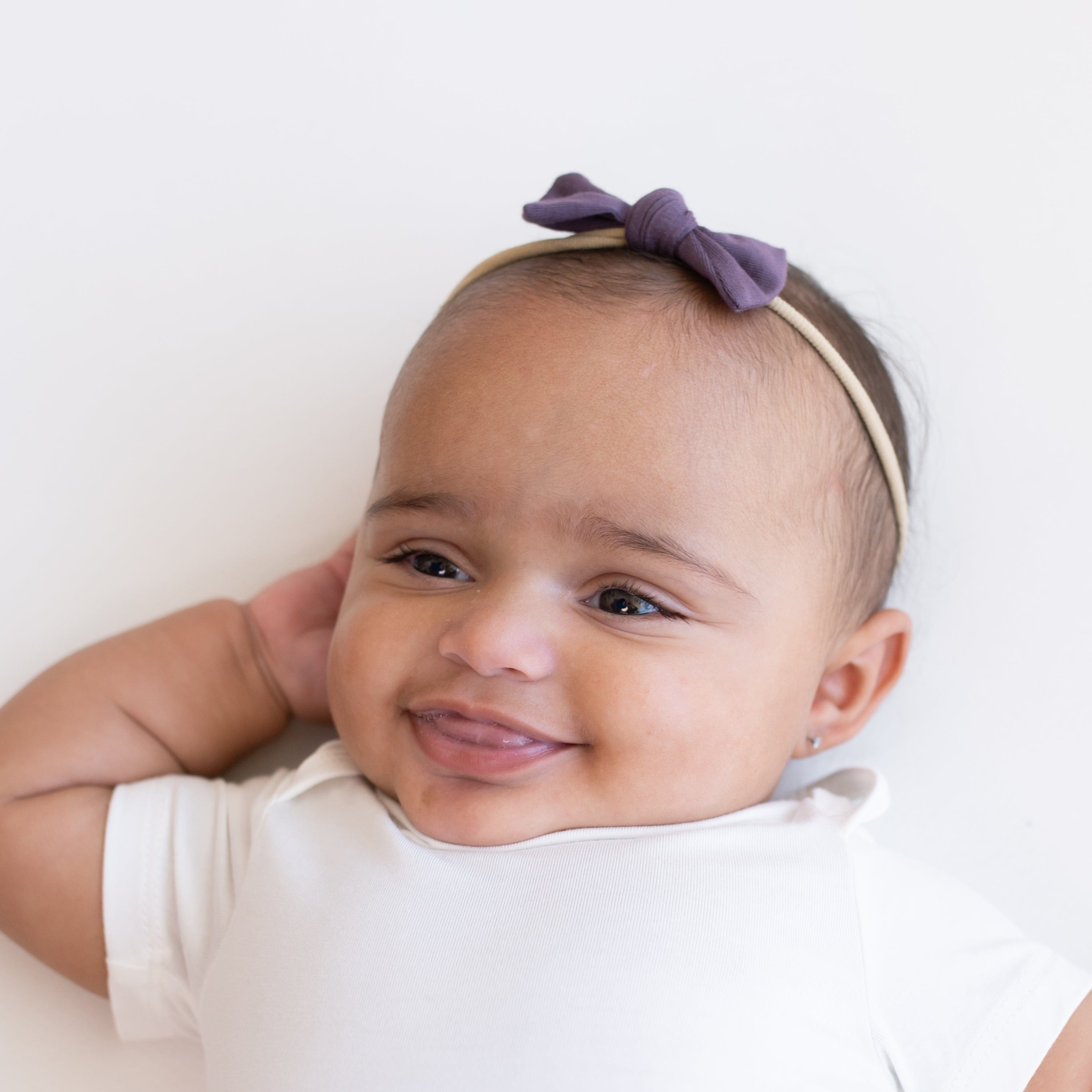 Infant wearing Kyte Baby Tiny Nylon Bow in Currant