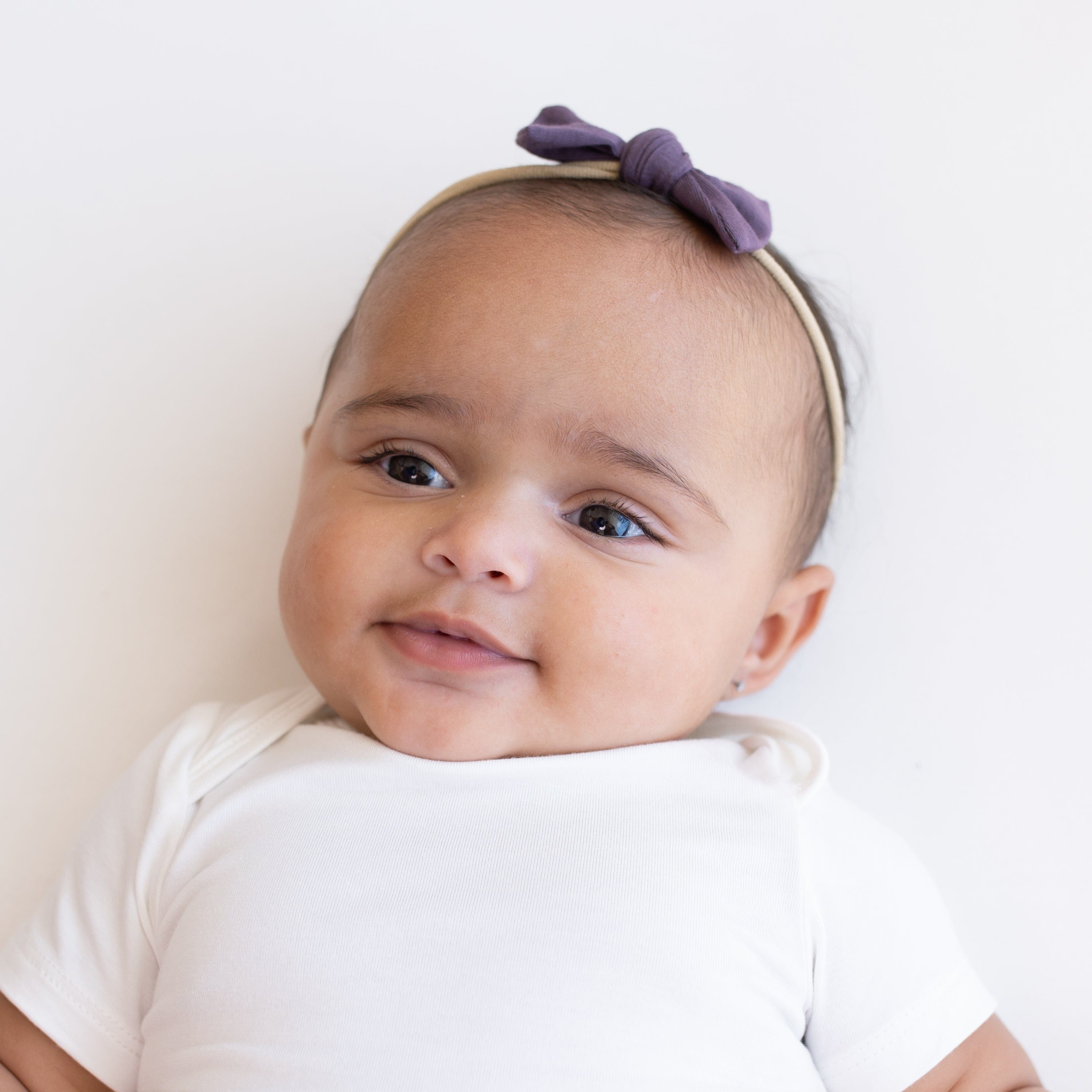 Infant wearing Kyte Baby Tiny Bow with Nylon Band in Currant