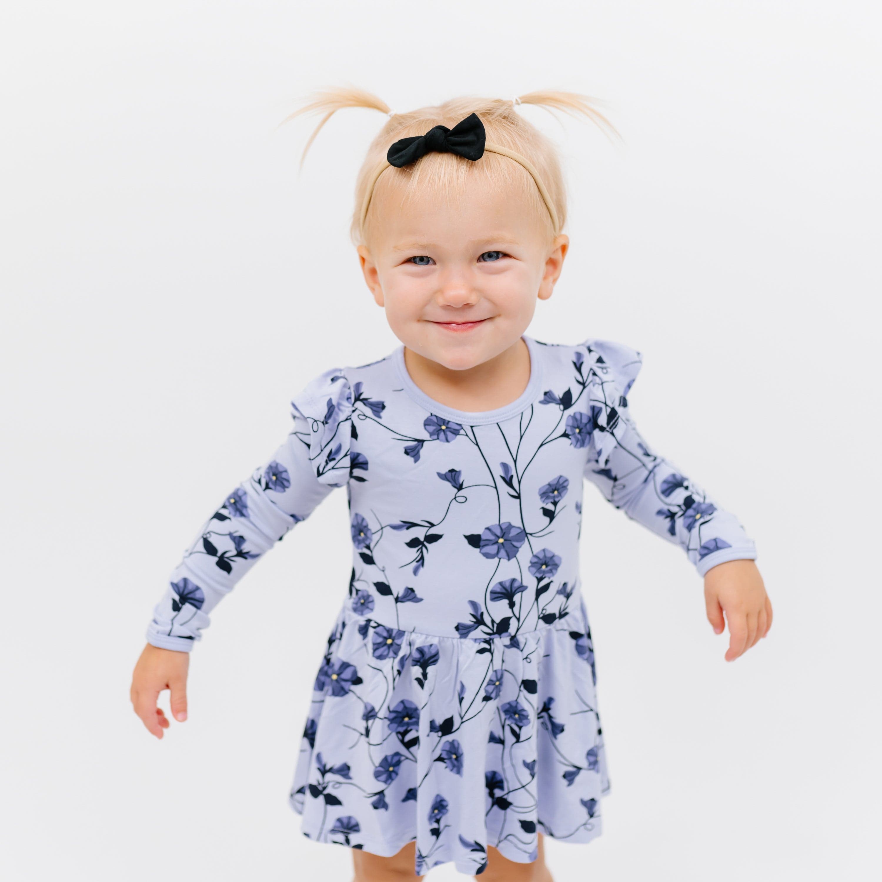Smiling toddler wearing Tiny Nylon Bow in Midnight and Long Sleeve Twirl Bodysuit in Petunia