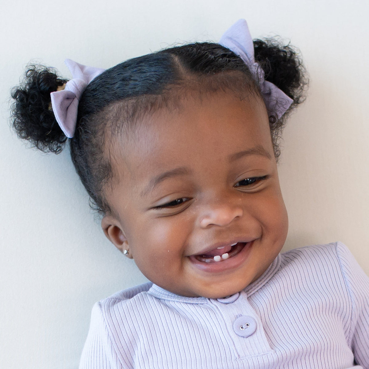 Smiling tddler wearing two Kyte Baby Tiny Nylon Bows in Taro in their pigtails