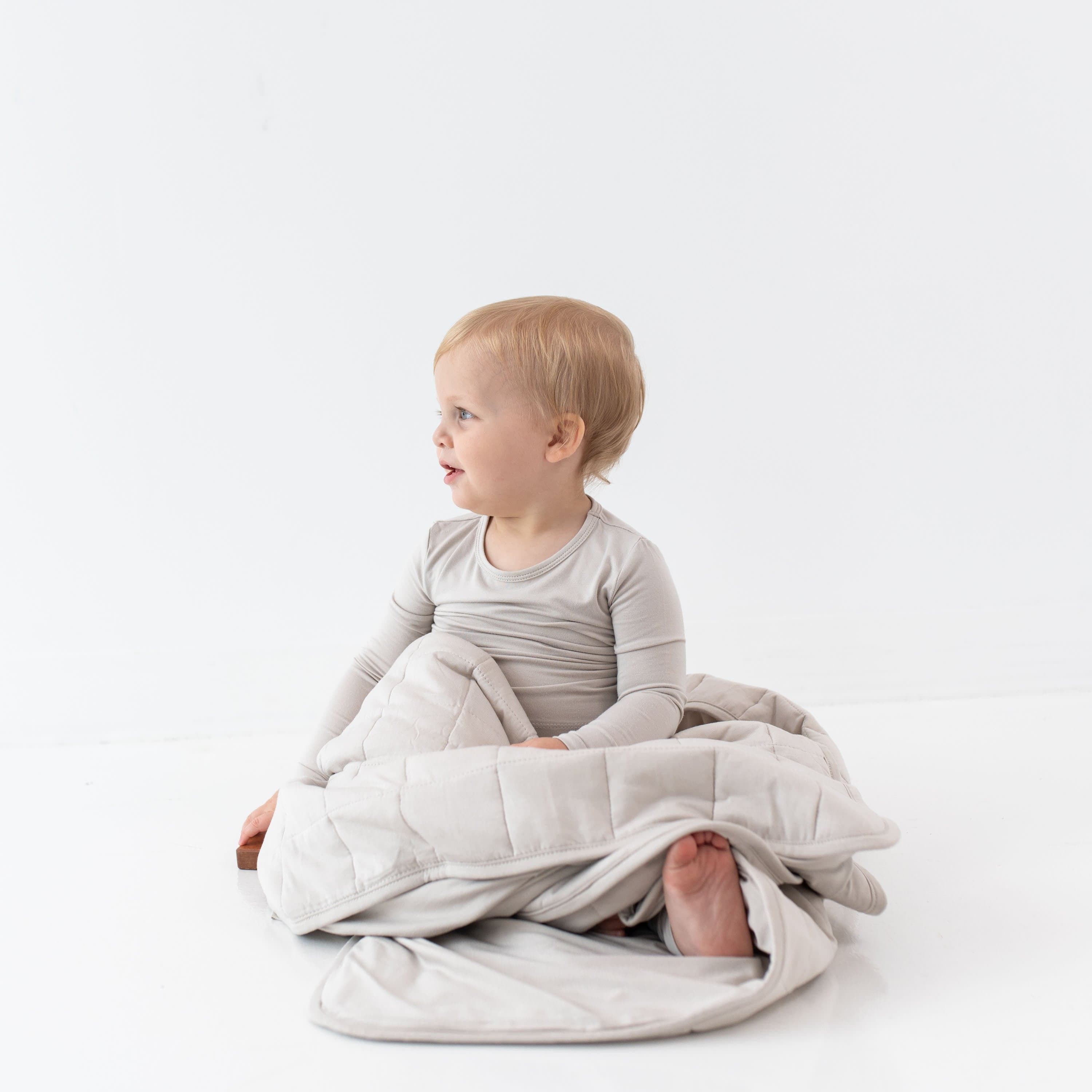 Child sitting while wrapped in a Toddler Blanket in Oat 1.0 TOG and matching Long Sleeve Pajama Set
