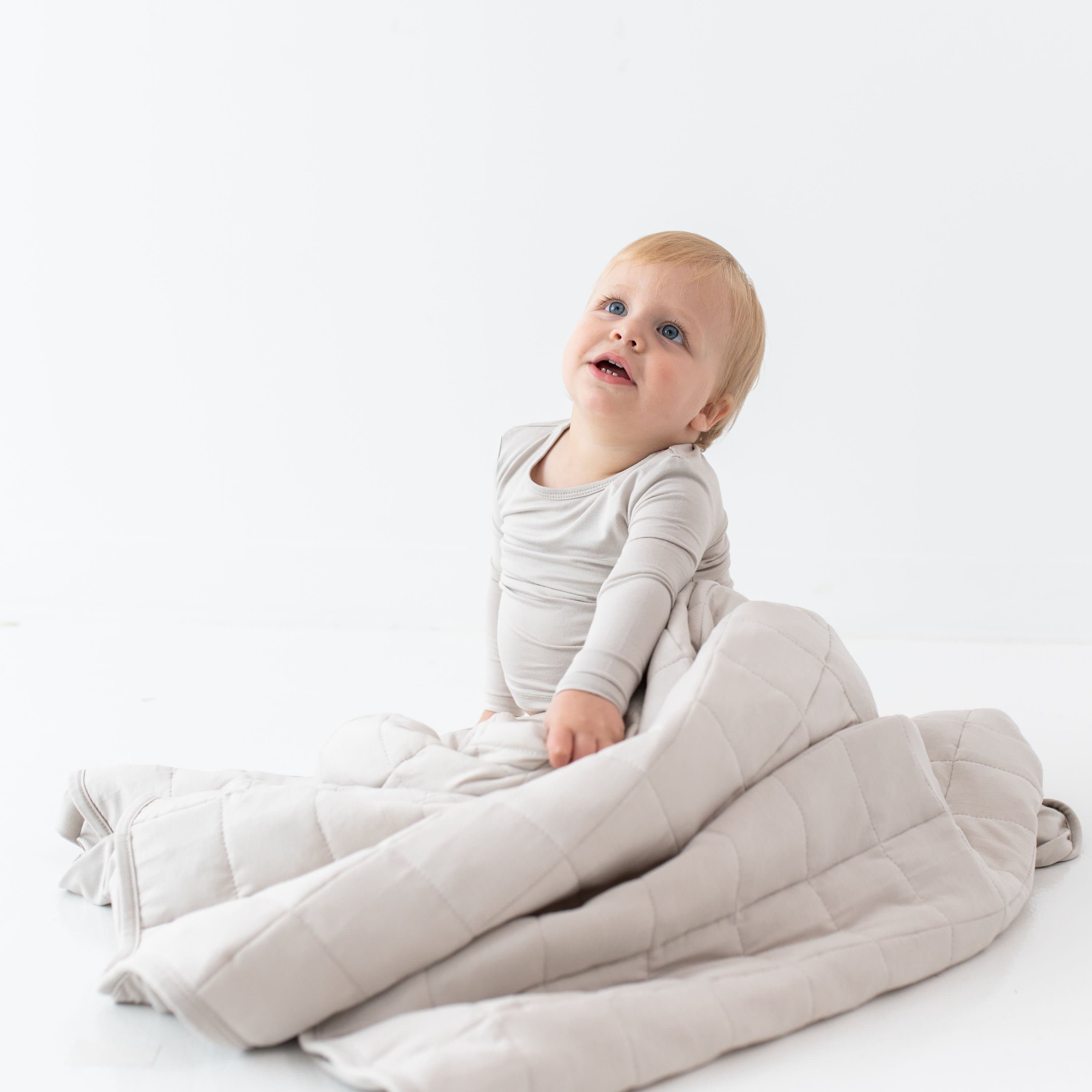 Child sitting while wrapped in a Toddler Blanket in Oat 1.0 TOG
