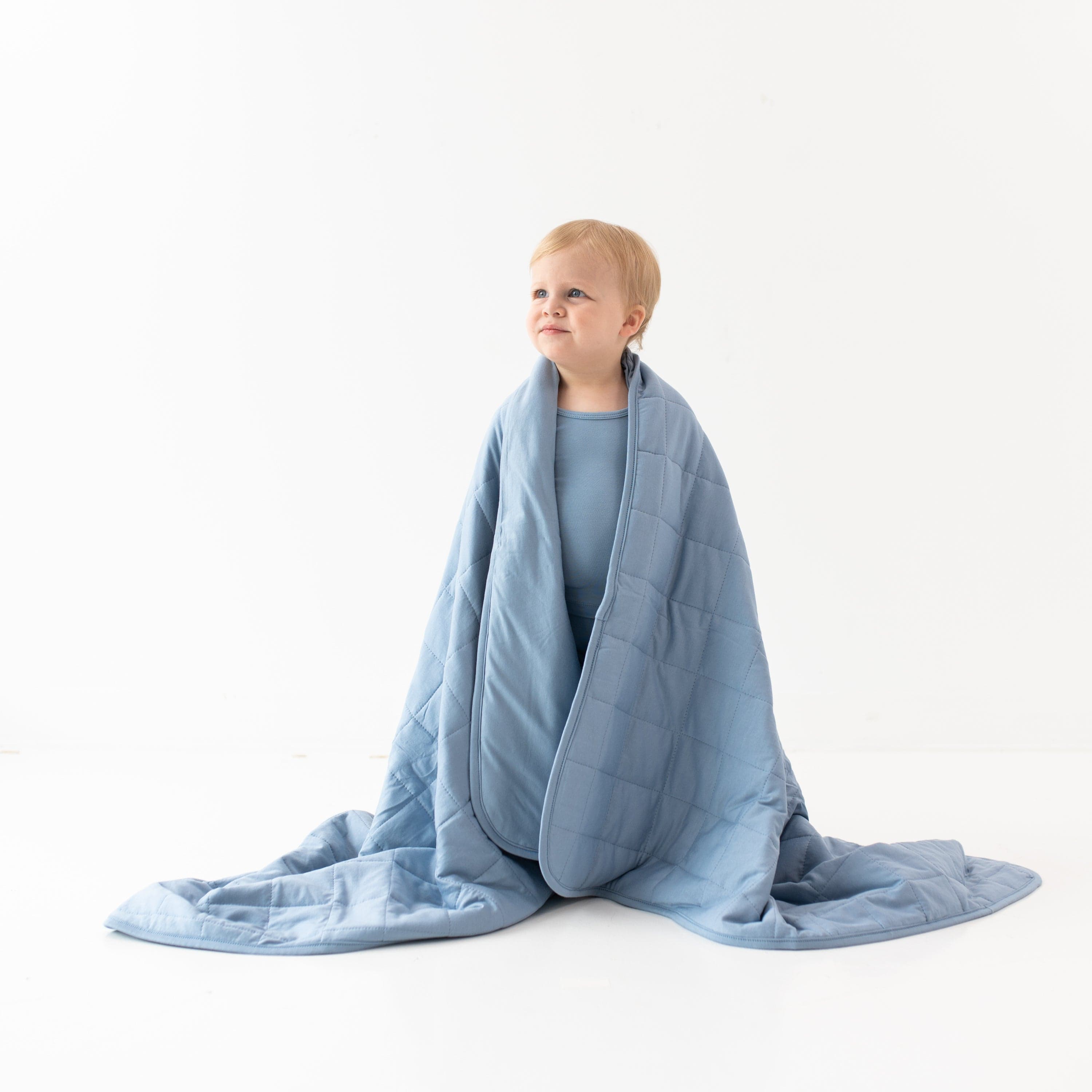 Child wrapped in Kyte Baby TOG 1.0 Toddler Blanket in Slate gray blue
