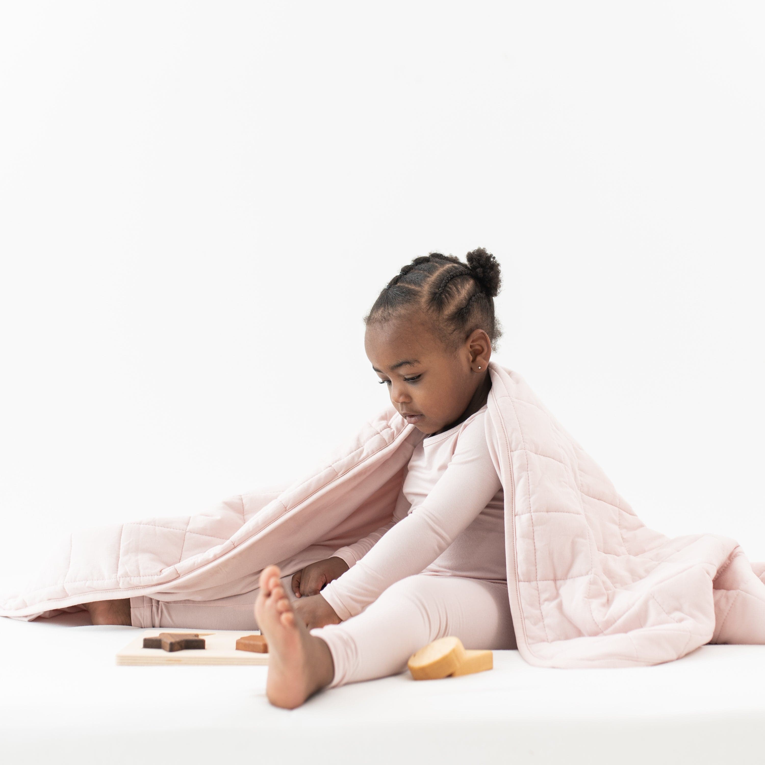 Sitting toddler wrapped in TOG 2.5 Toddler Blanket in Blush and wearing matching long sleeve pajama set