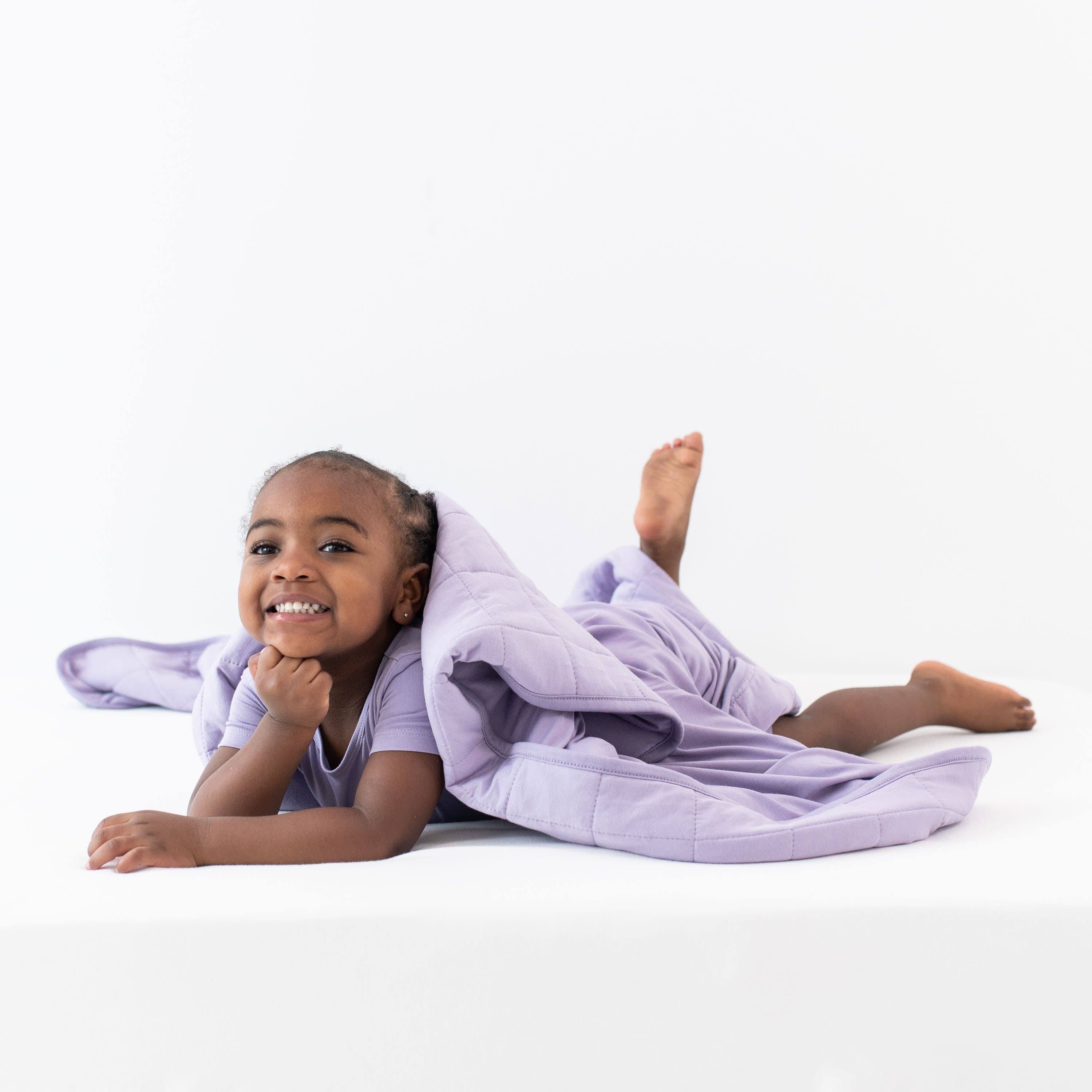 Smiling child wrapped in Kyte Baby Toddler Blanket in Taro 2.5