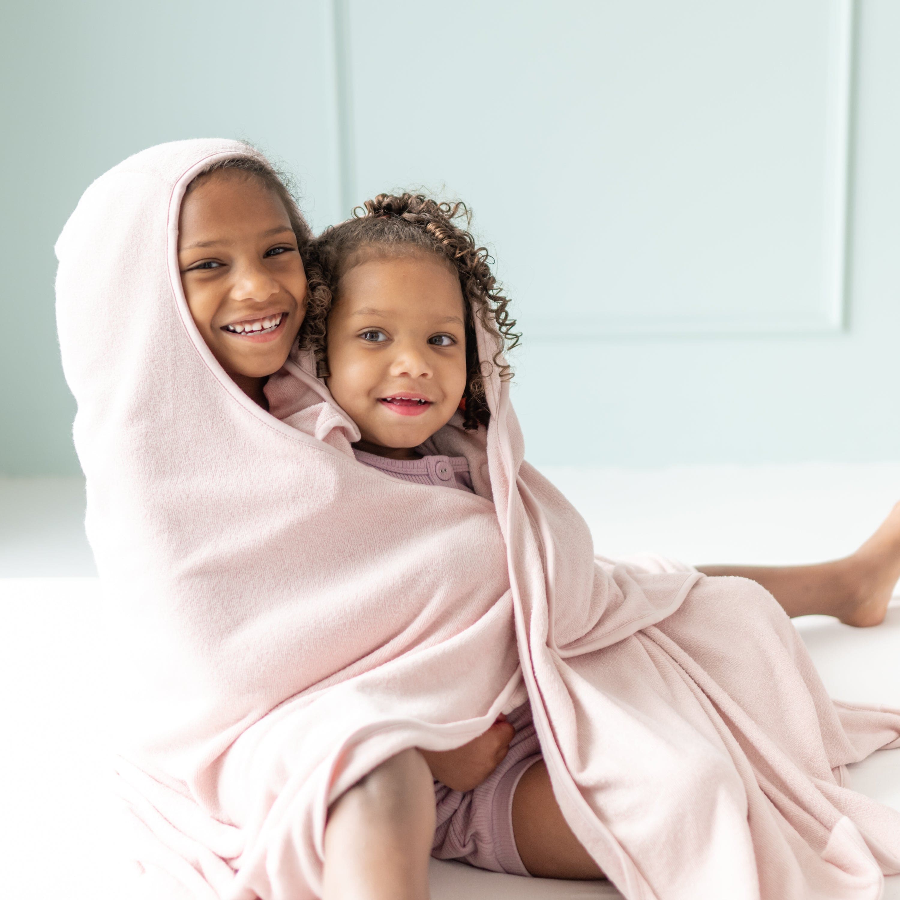 Siblings wrapped in Kyte Baby Toddler Hooded Bath Towel in Blush