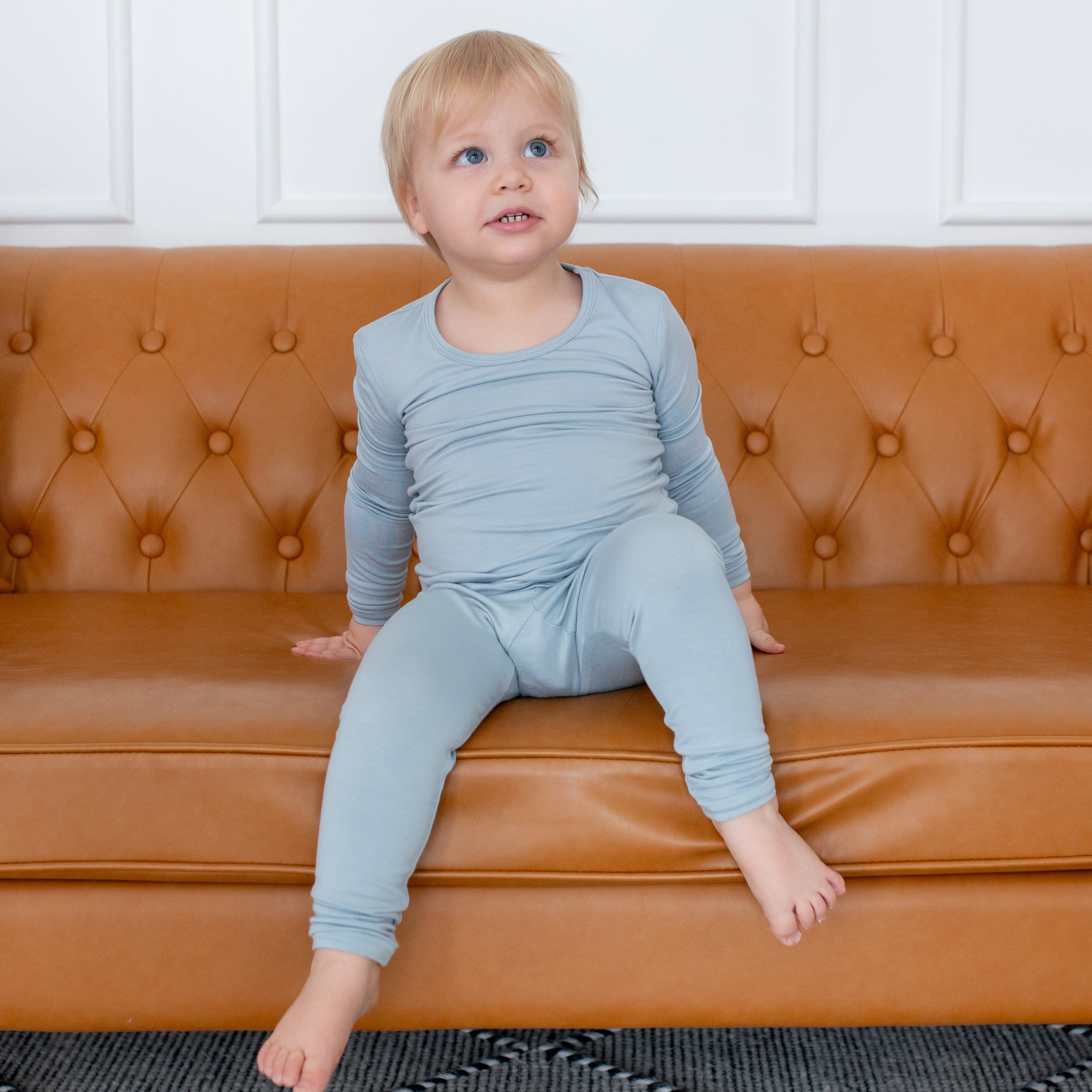 Toddler wearing Long Sleeve Pajama Set in Fog sitting on a tan colored leather couch