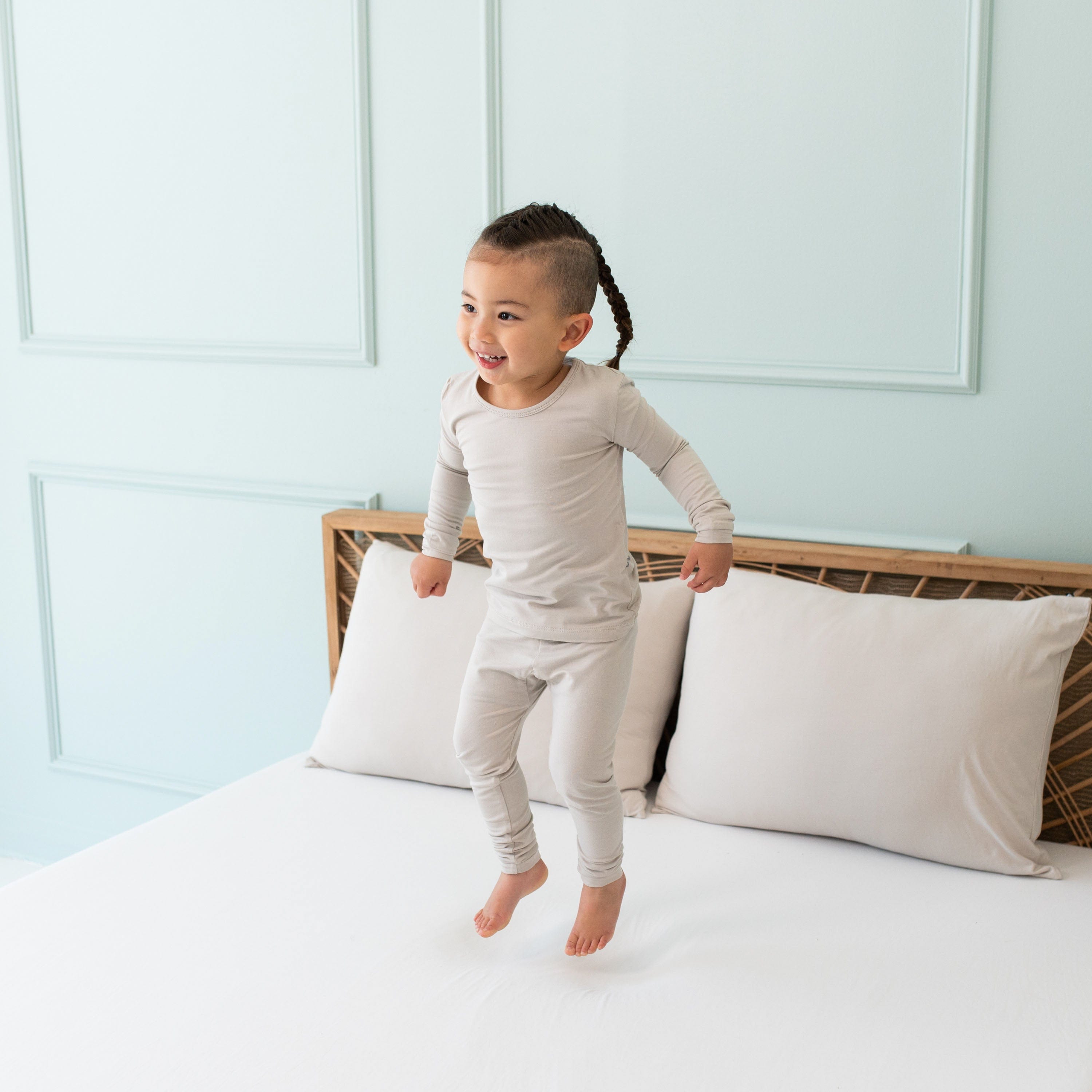 Toddler jumping in a bed while wearing Long Sleeve Kids Pajamas in Oat
