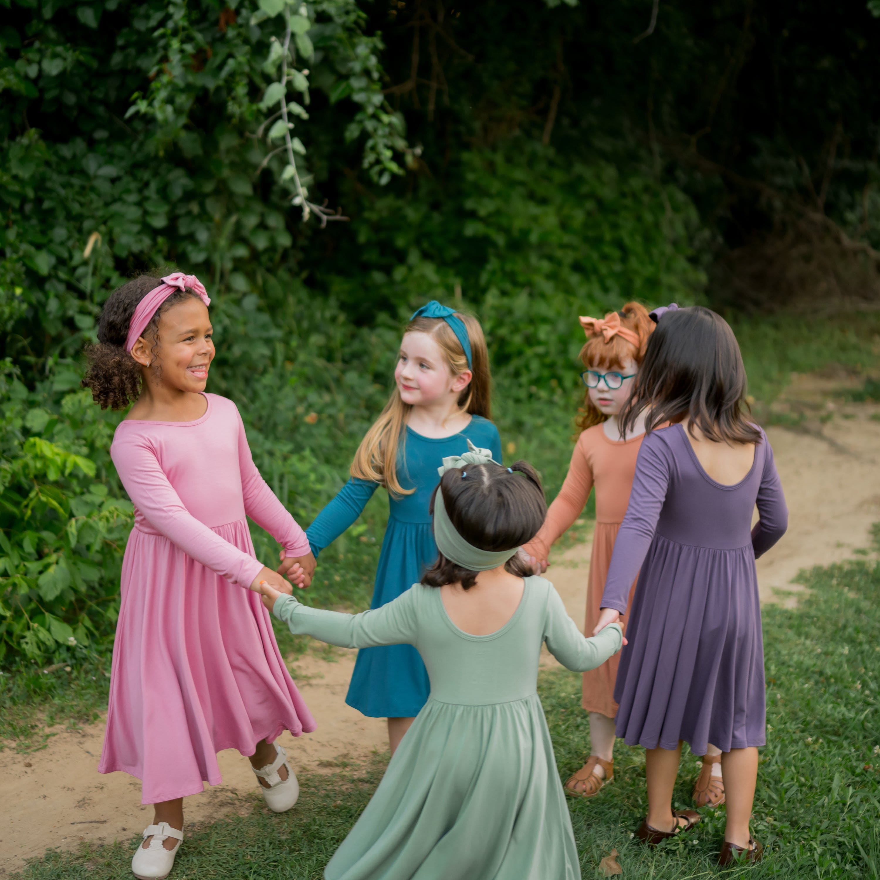 Group of 5 girls holding hands and walking around in a circle in a field wearing various colors in the Long Sleeve Twirl Dresses