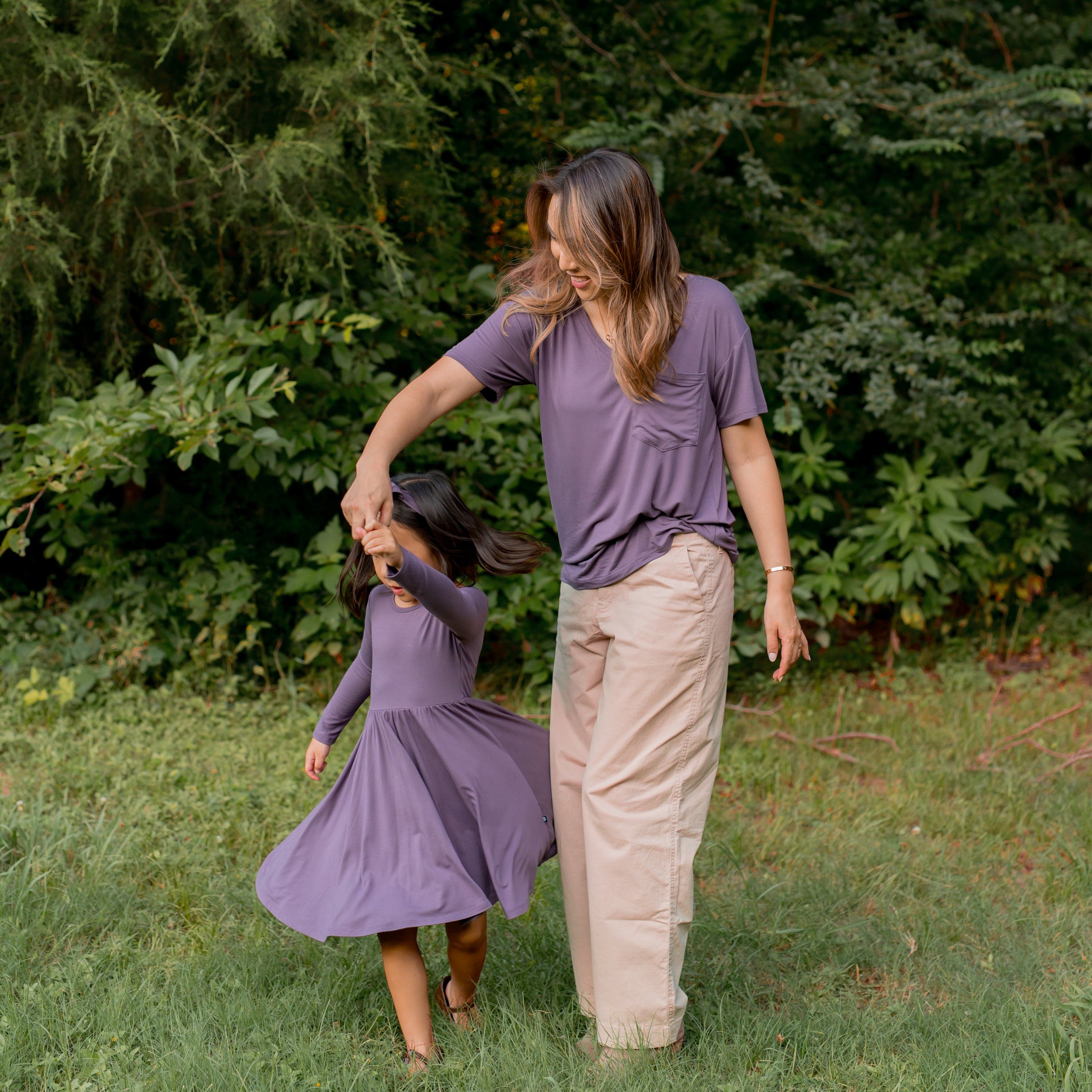 Mother wearing the Women's V-Neck in Currant standing in the grass twirling her daughter who is wearing the Long Sleeve Twirl Dress in Currant