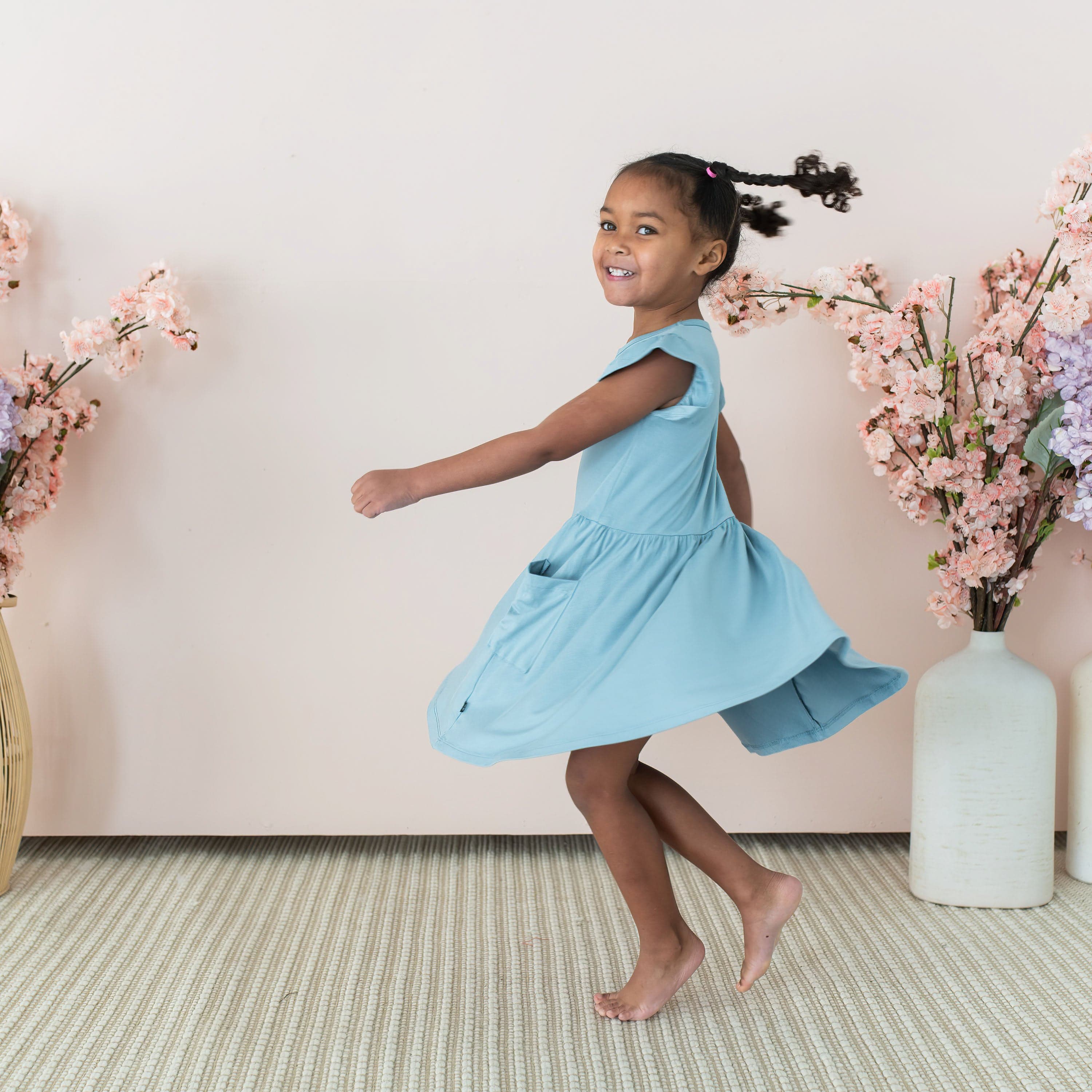 Toddler twirling in Kyte Baby bamboo Pocket Dress in Dusty Blue