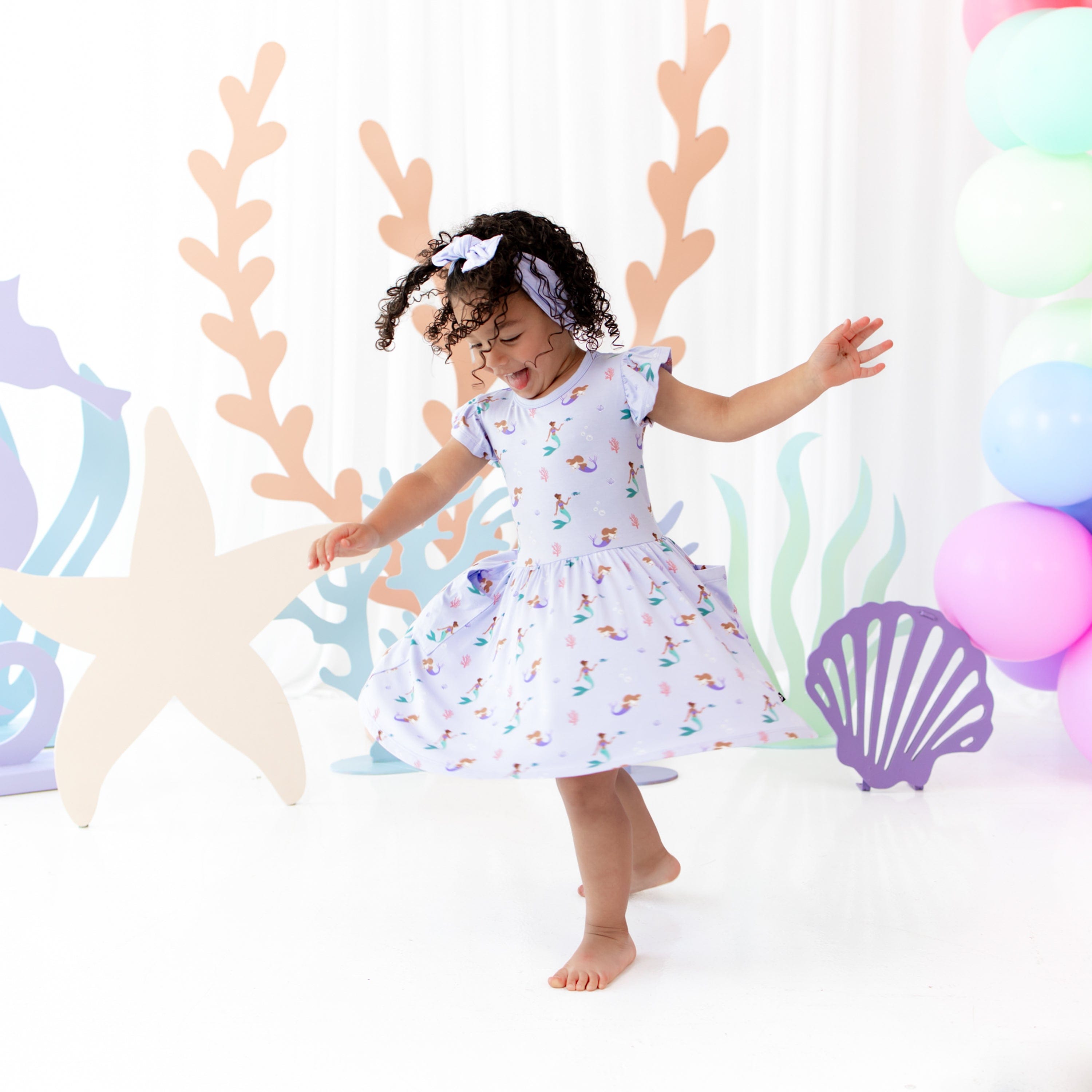 Toddler twirling in Kyte Baby bamboo Pocket Dress in Mermaid