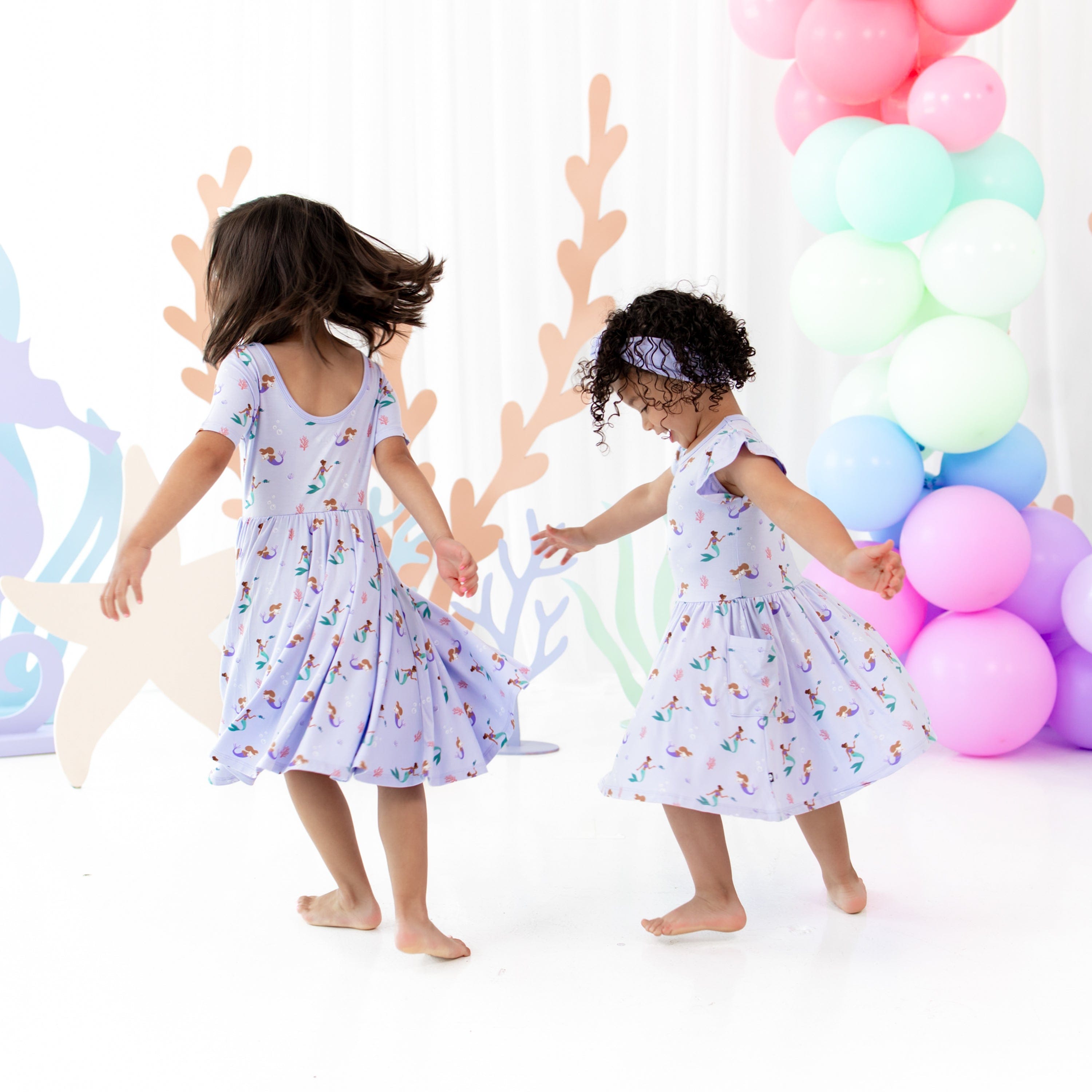 Girls twirling in matching Kyte Baby Dresses in Mermaid