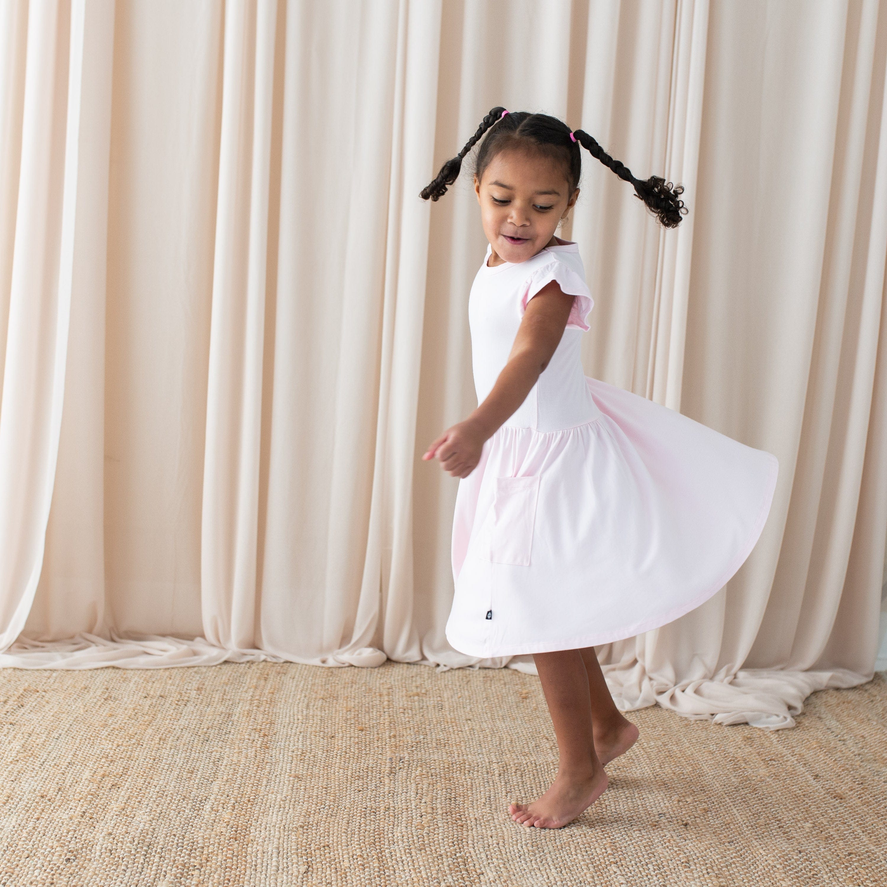 Toddler twirling in Kyte Baby bamboo Pocket Dress in Sakura pink
