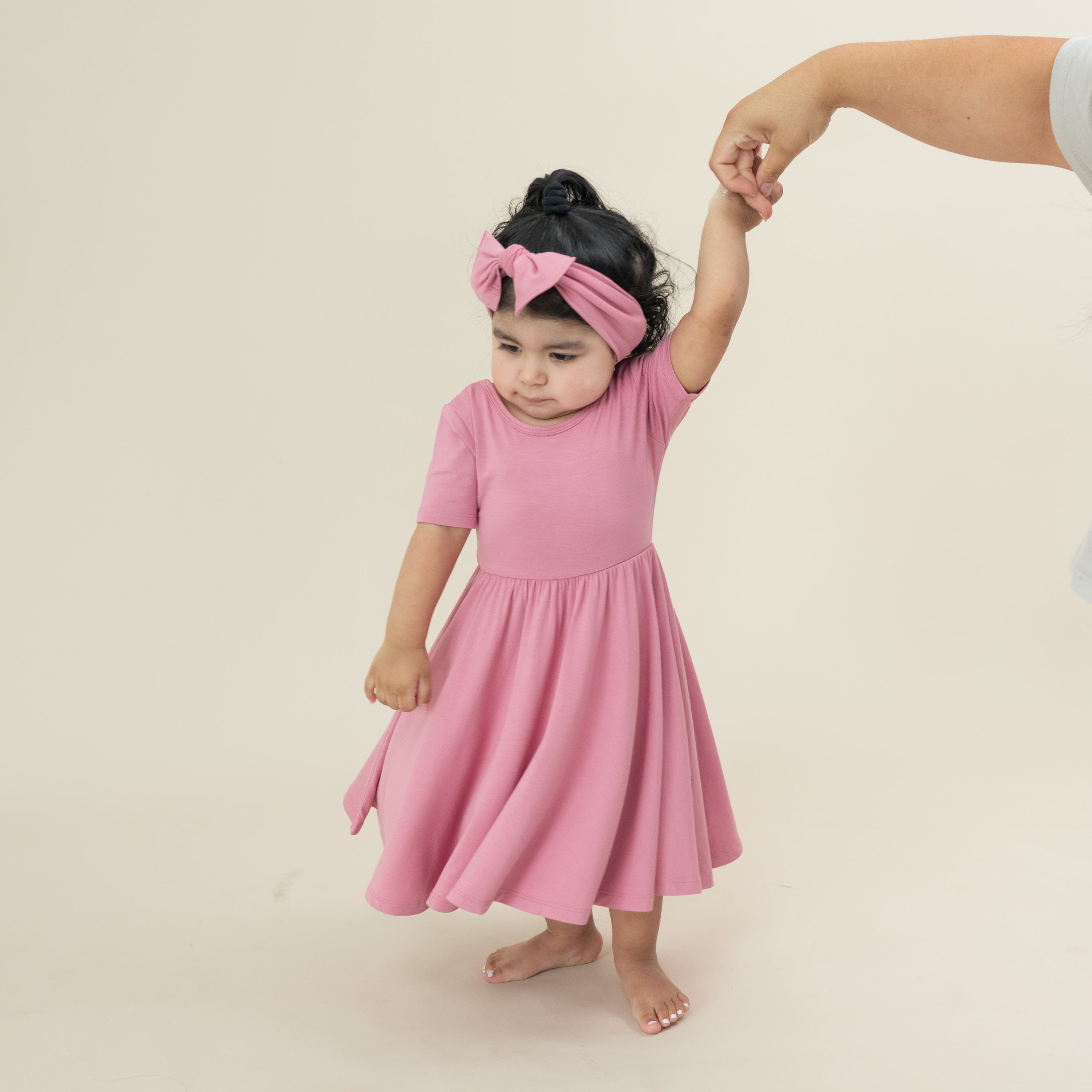 Young girl twirling wearing the Twirl Dress in Apple Blossom and matching knotted bow headband