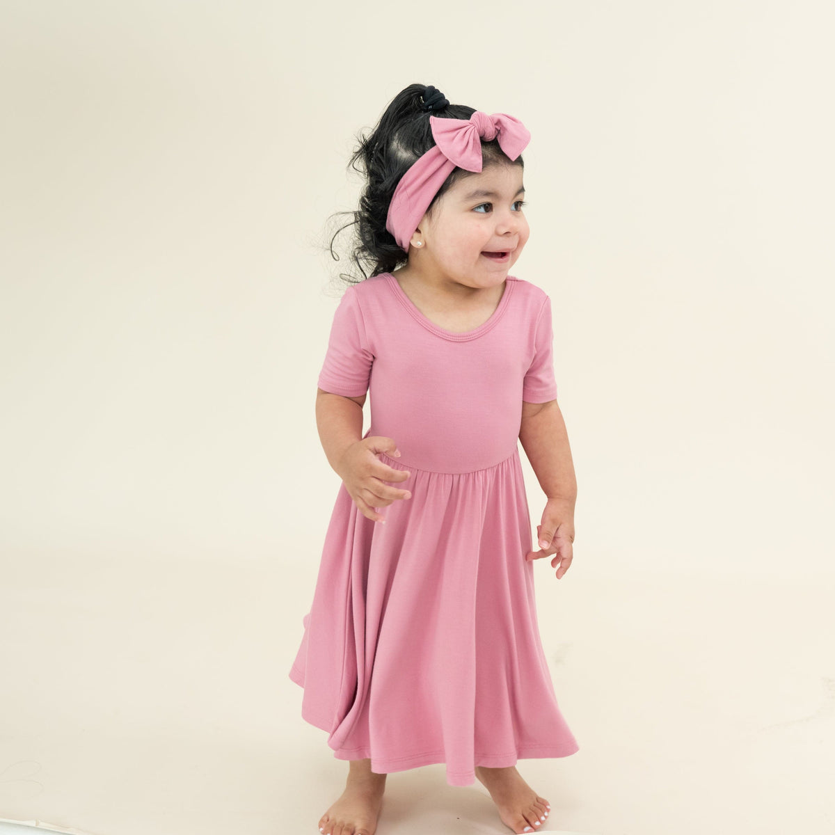 Young girl wearing the Twirl Dress in Apple Blossom with matching knotted bow headband