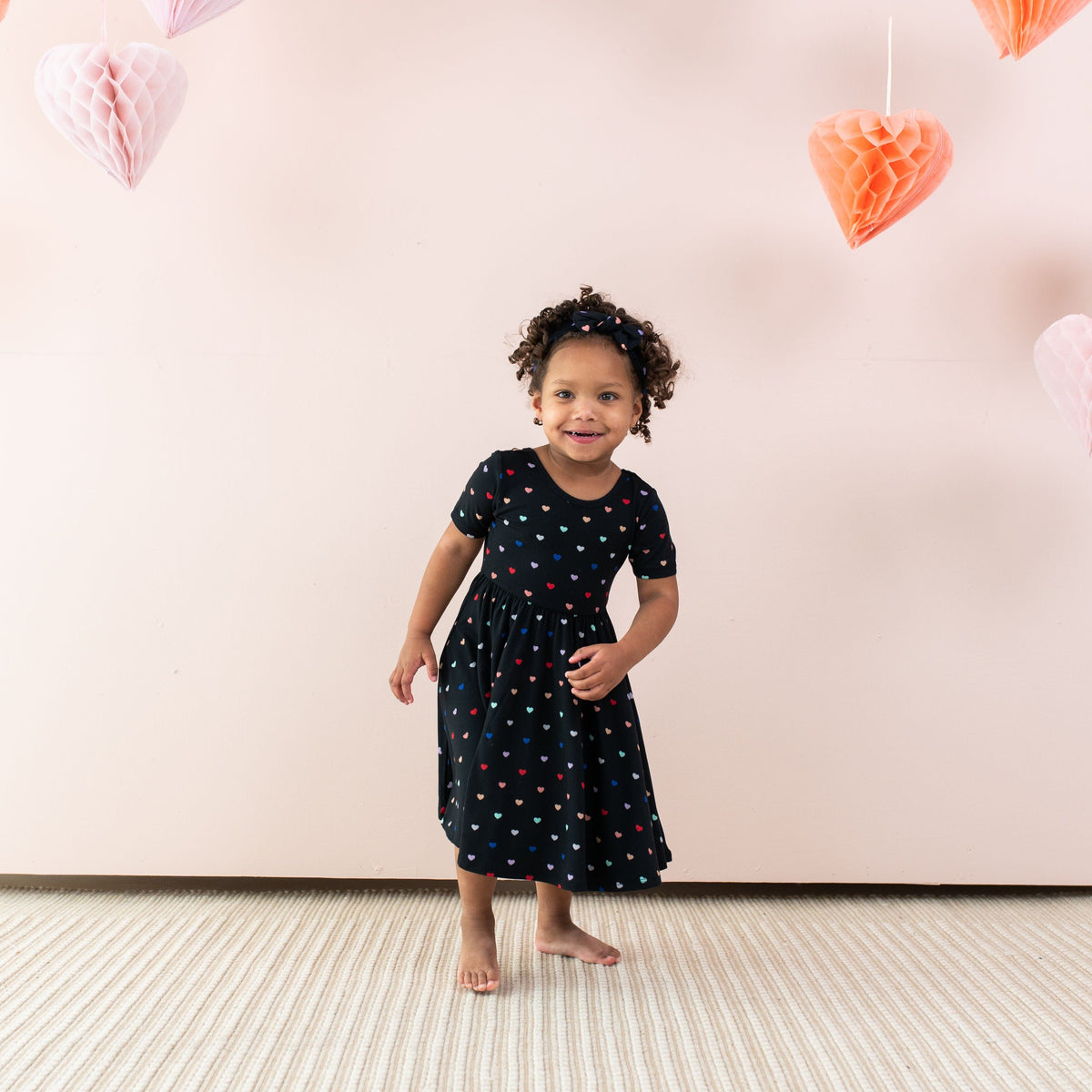 Girl wearing Kyte Baby Twirl Dress in Midnight Rainbow Heart