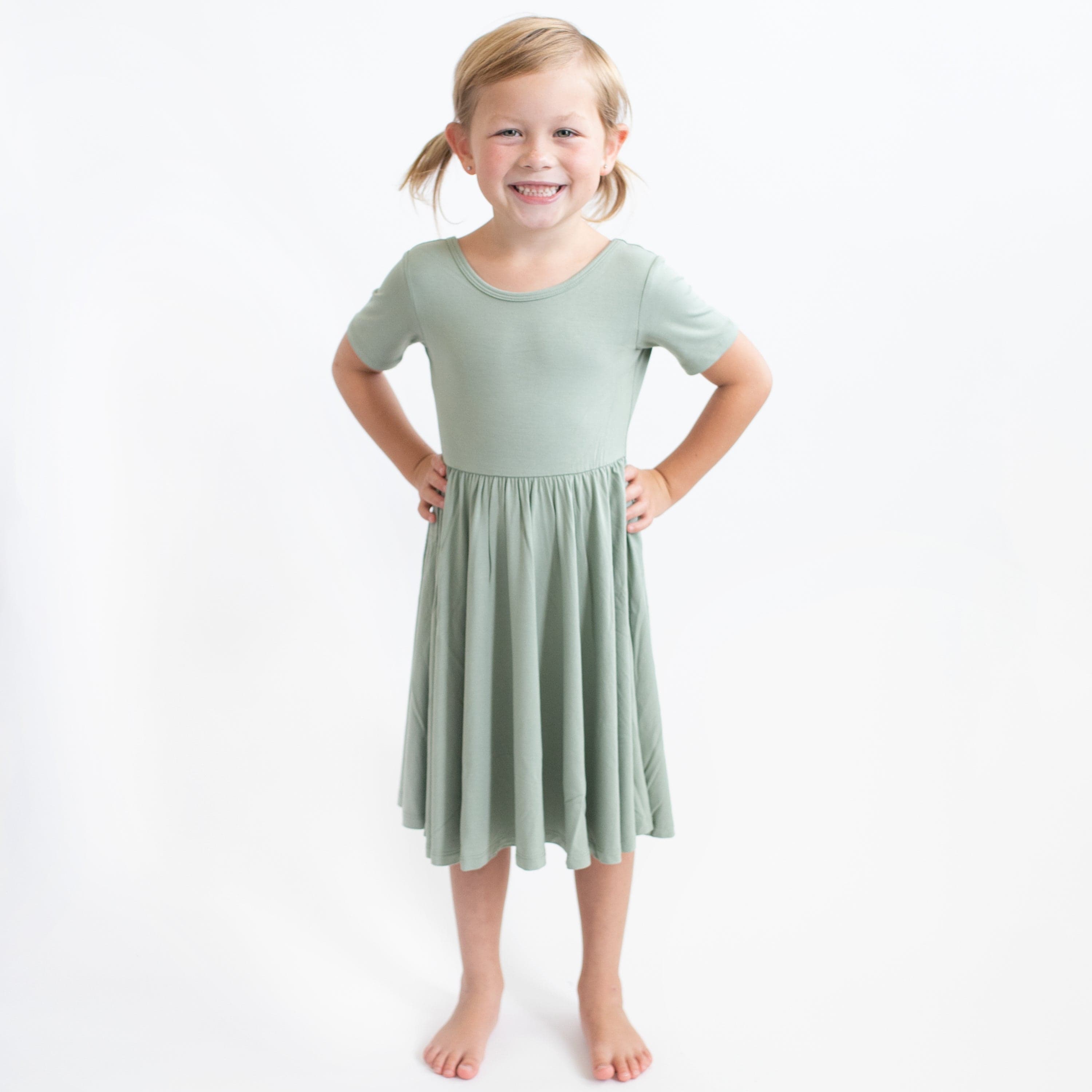 Young girl modeling the Twirl Dress in Thyme standing with both hands on her hips