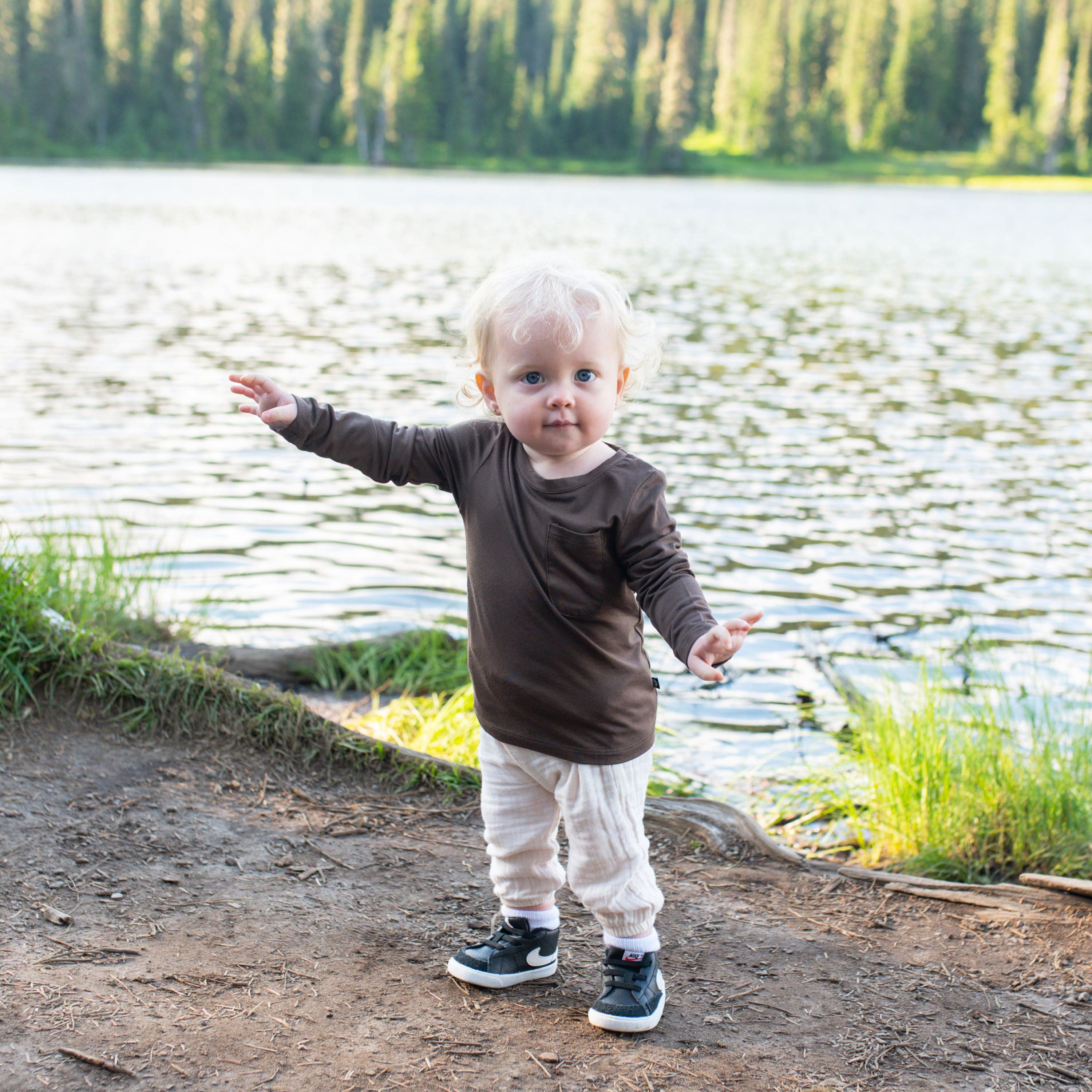 Toddler standing on a path near the water wearing the Long Sleeve Toddler Crew Neck Tee in Espresso