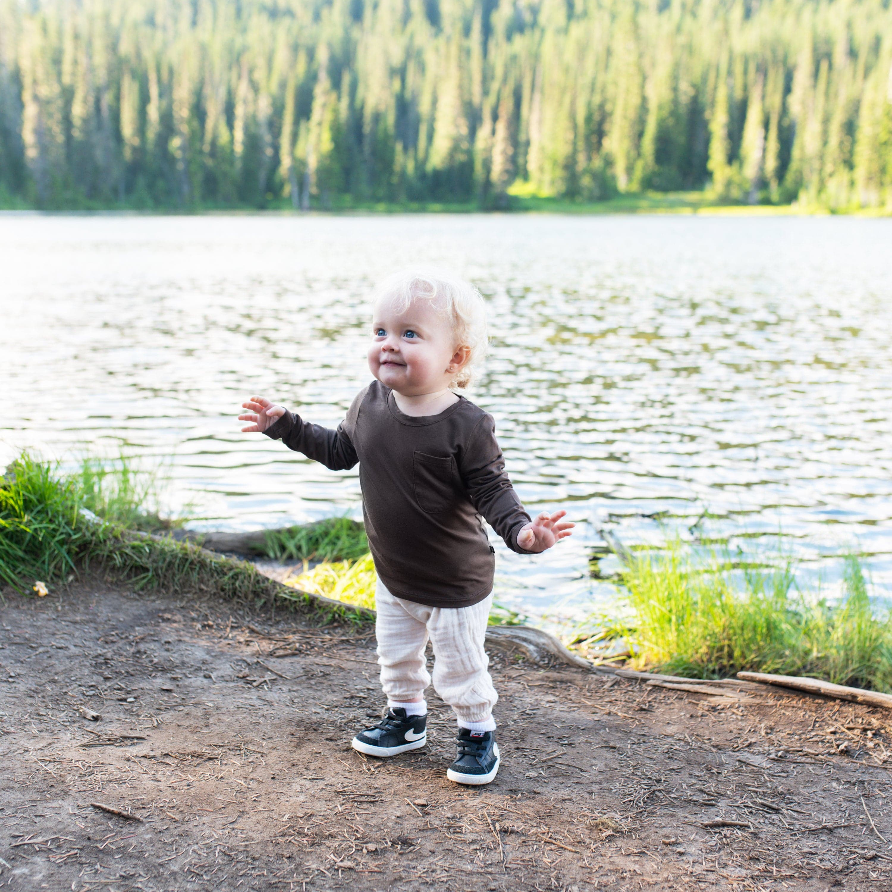 Toddler standing on a path near the water wearing the Long Sleeve Toddler Crew Neck Tee in Espresso