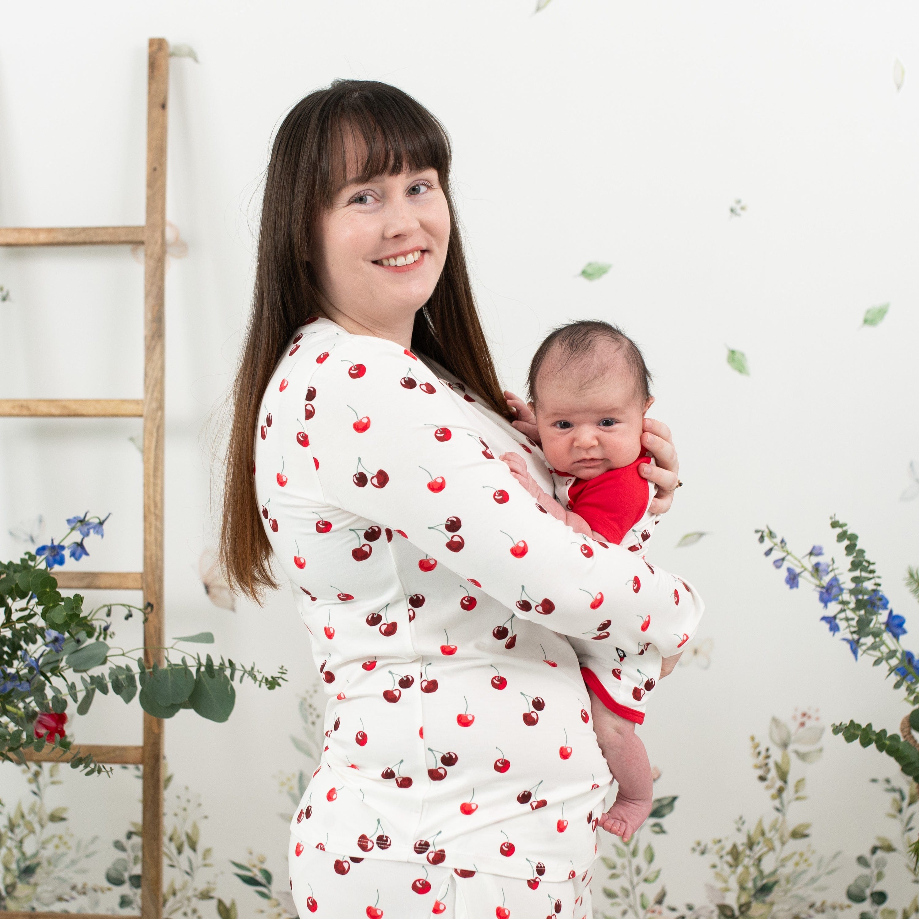Woman wearing Kyte Baby women's jogger pajama set with matching newborn outfit in Cherry