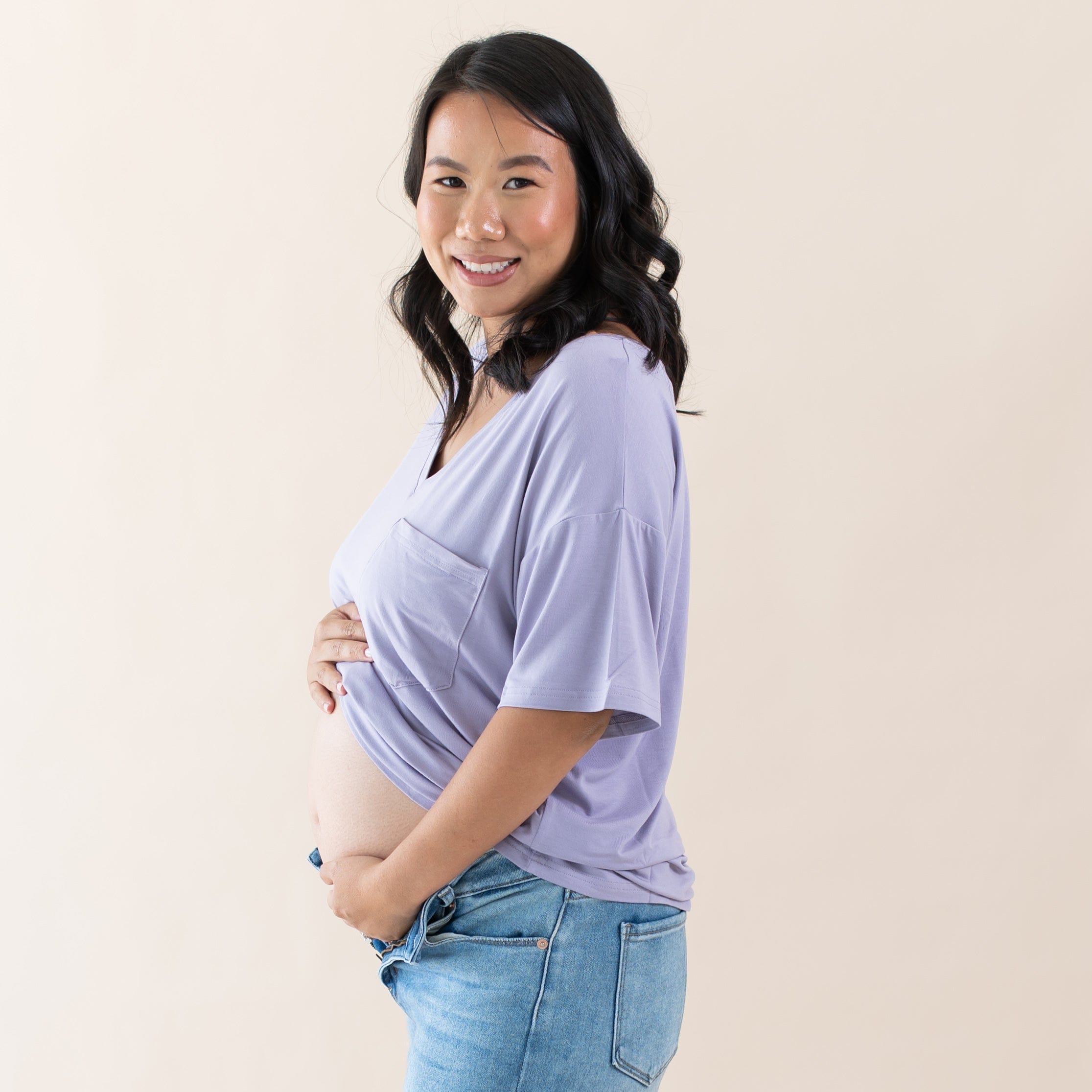Expectant mother cradling her baby bump wearing the Women’s Relaxed Fit V-Neck in Taro paired with jeans