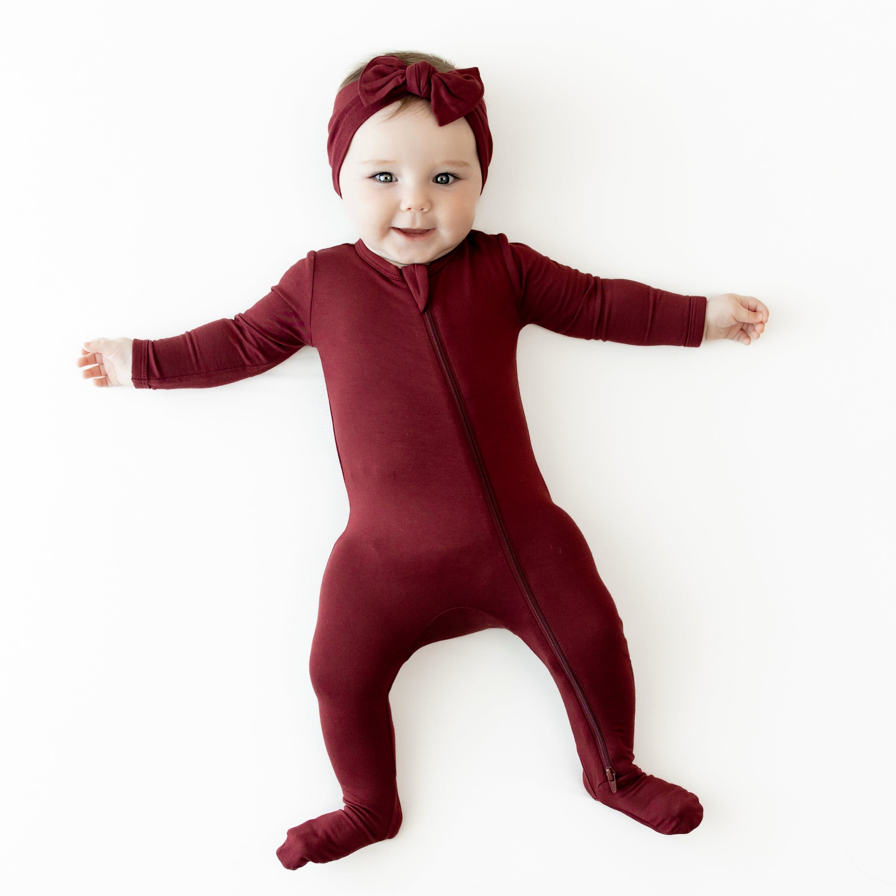 Infant wearing Zippered Footie pjs in Burgundy with matching knotted bow headband