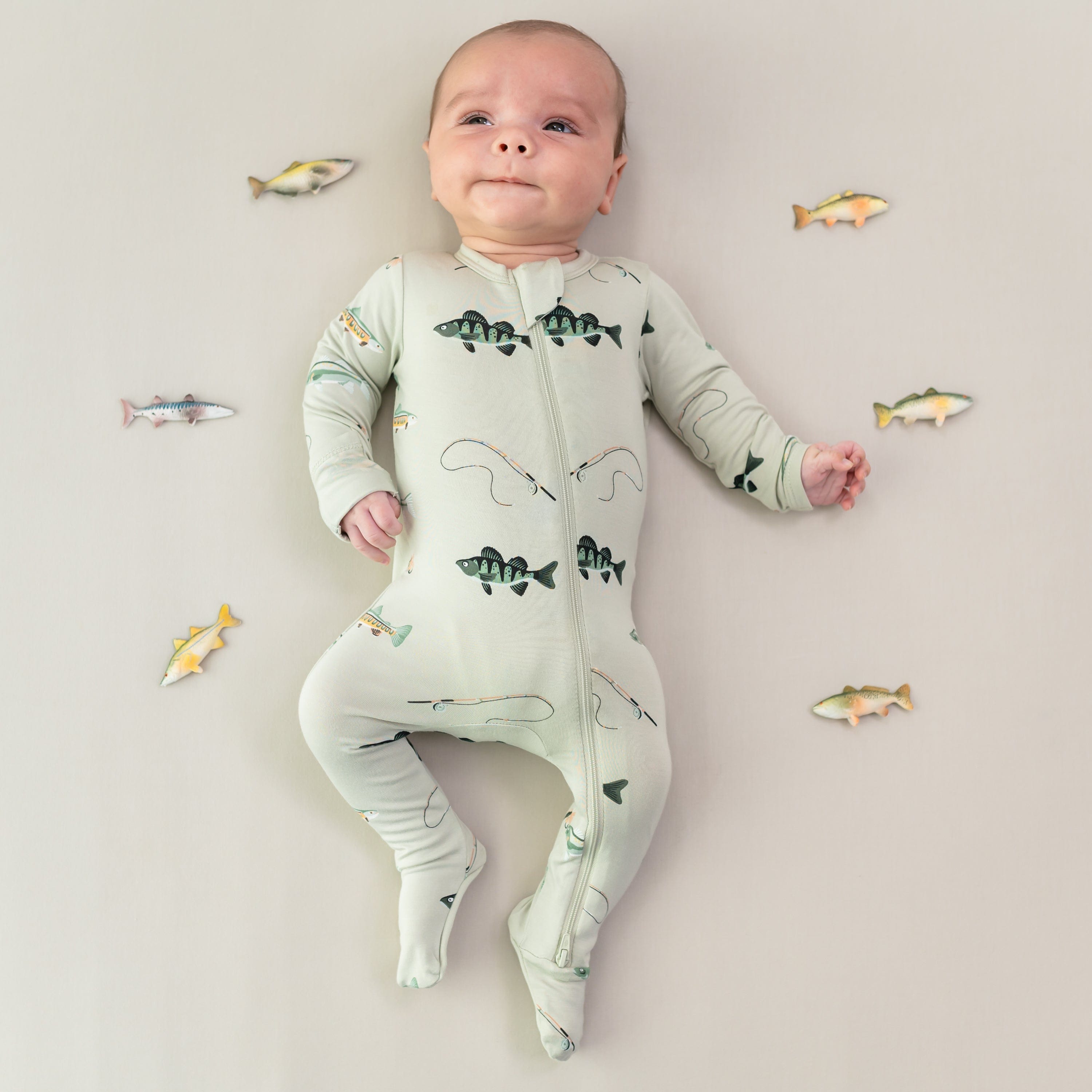 Infant looking up wearing the Zippered Footie in Fishing surrounded by toy fish