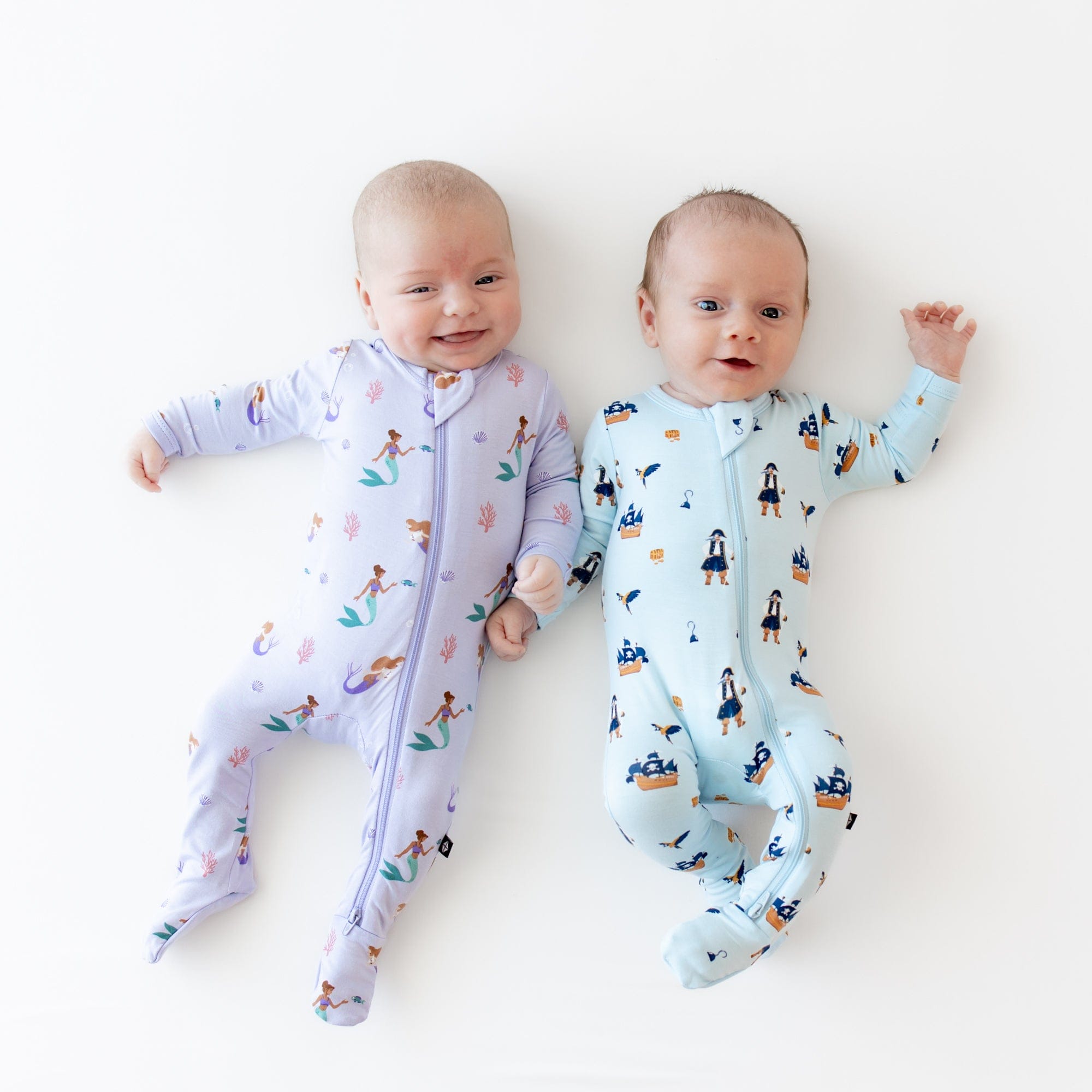Babies wearing Kyte Baby matching footie pajamas in Pirate and Mermaid