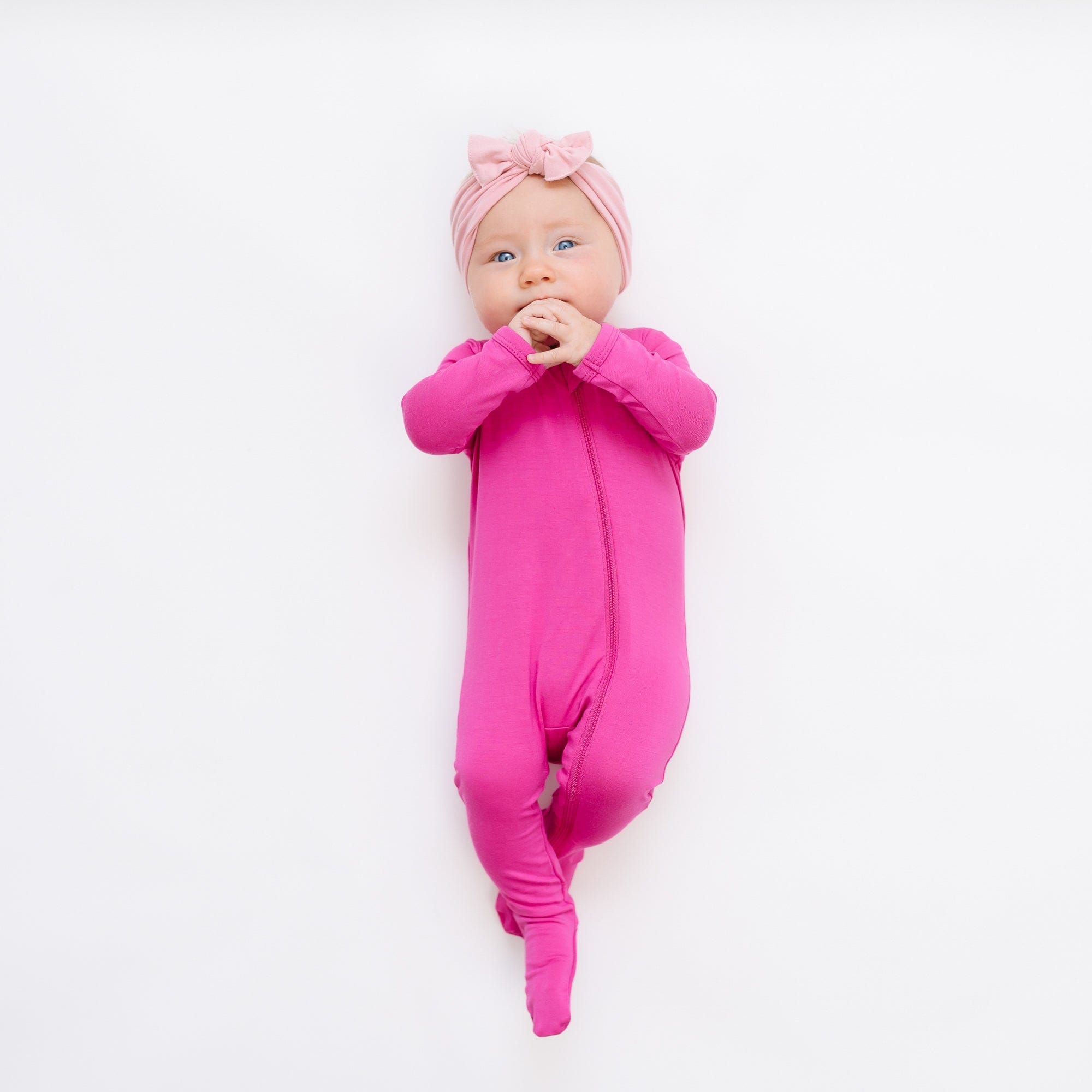 Infant wearing Kyte Baby Zippered Footie pajamas in Raspberry pink