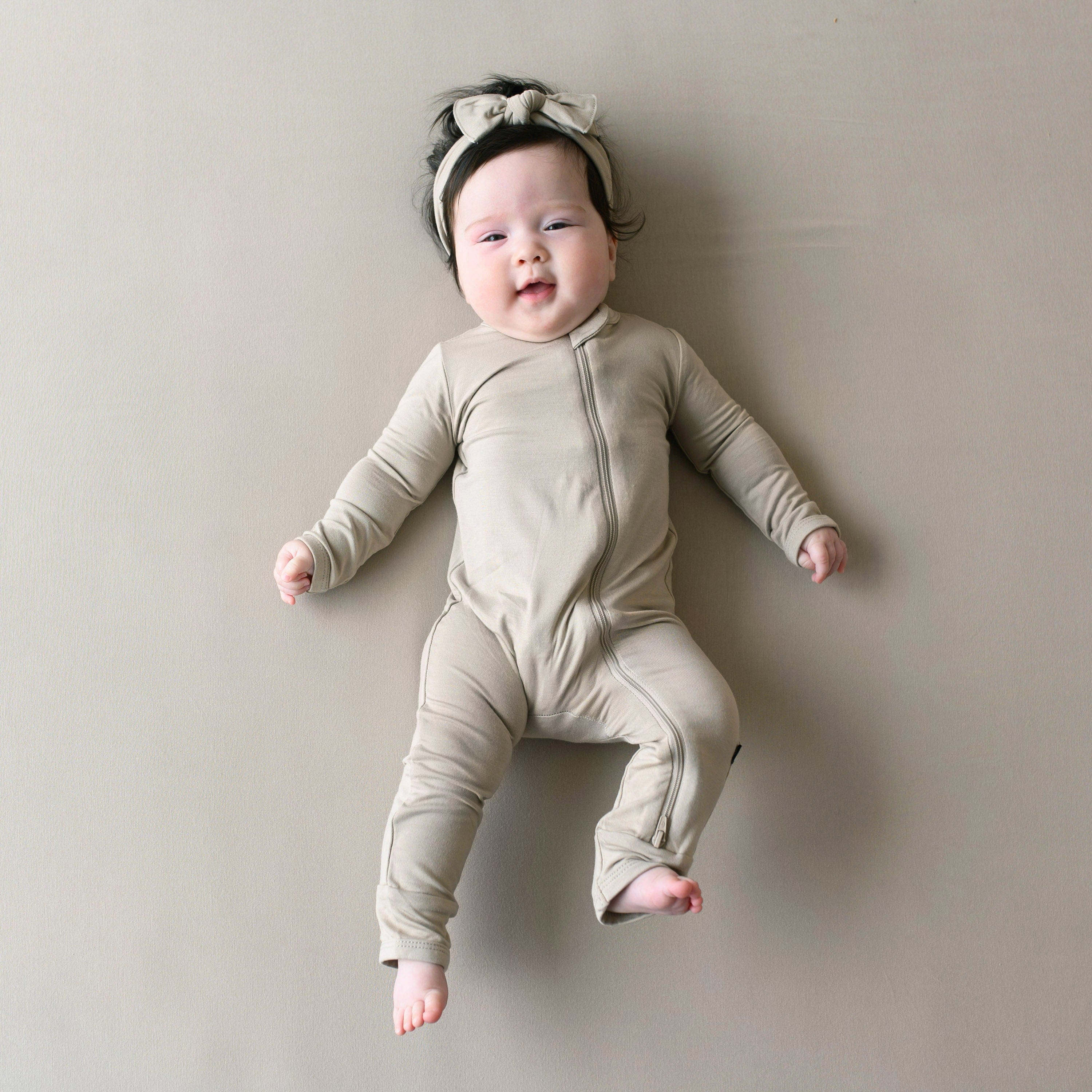 Infant wearing Zippered neutral Romper in Almond with matching knotted bow headband