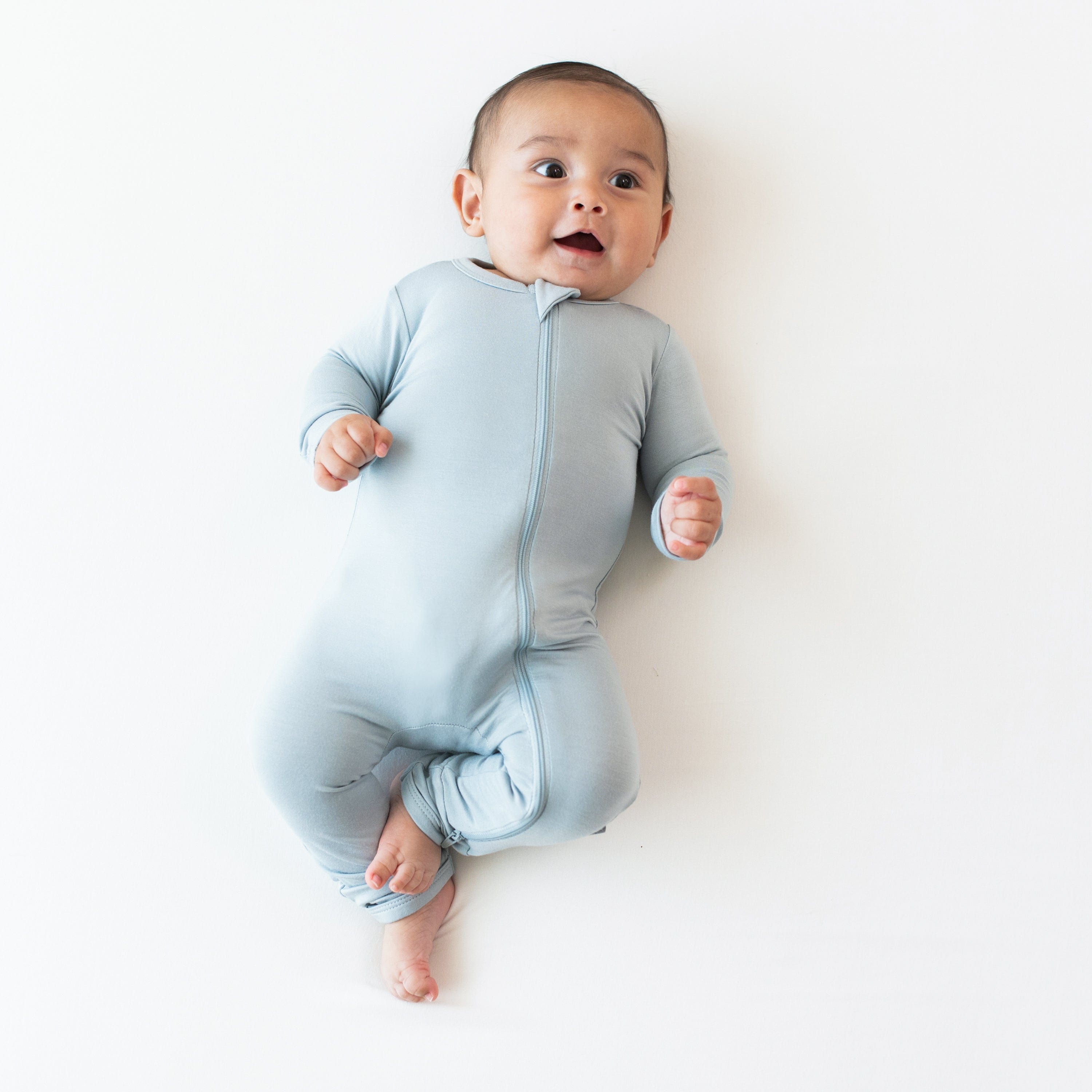 Baby laying on an off-white surface while wearing a Zippered Romper in Fog