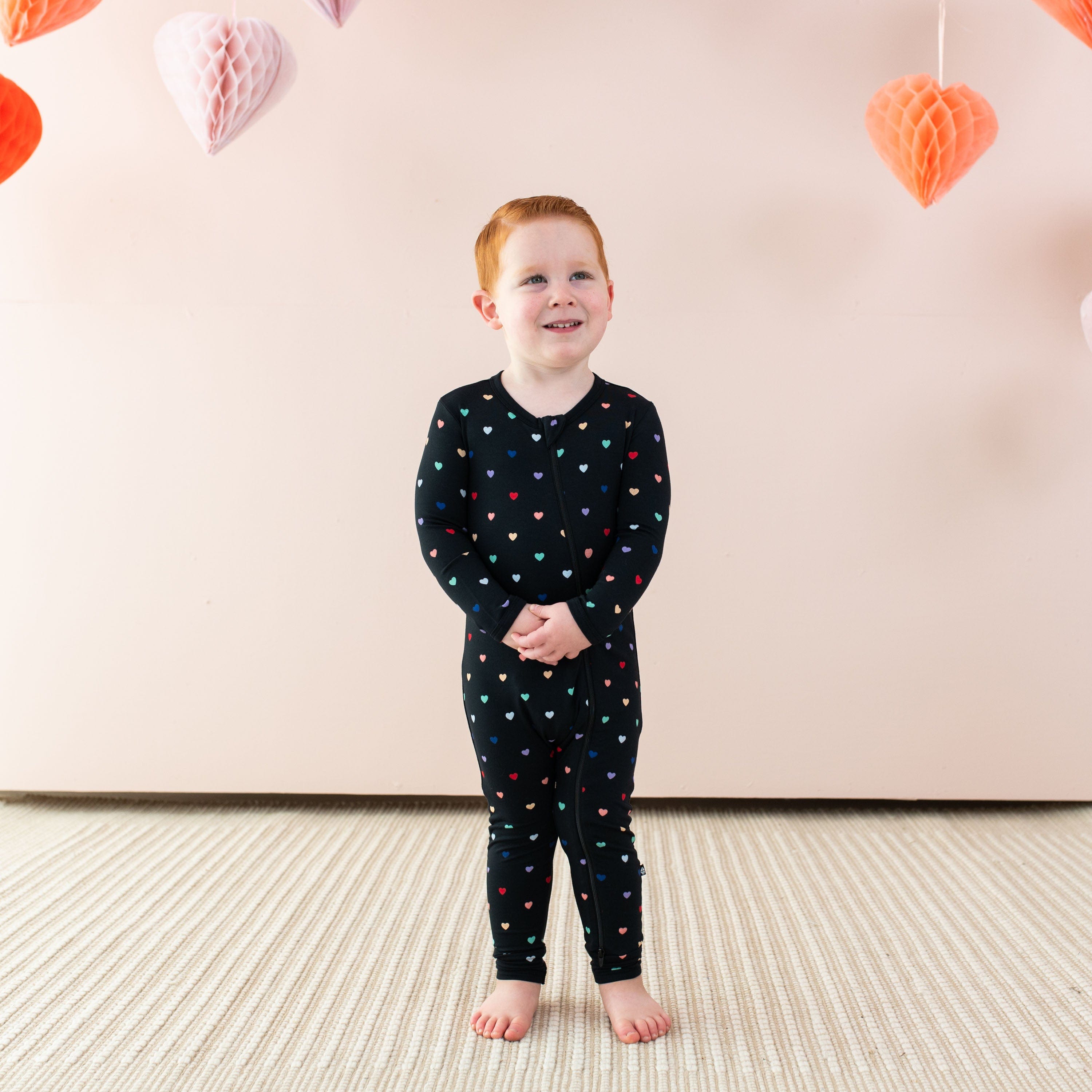 Toddler wearing Kyte Baby bamboo Zippered Romper pajamas in Midnight Rainbow Heart