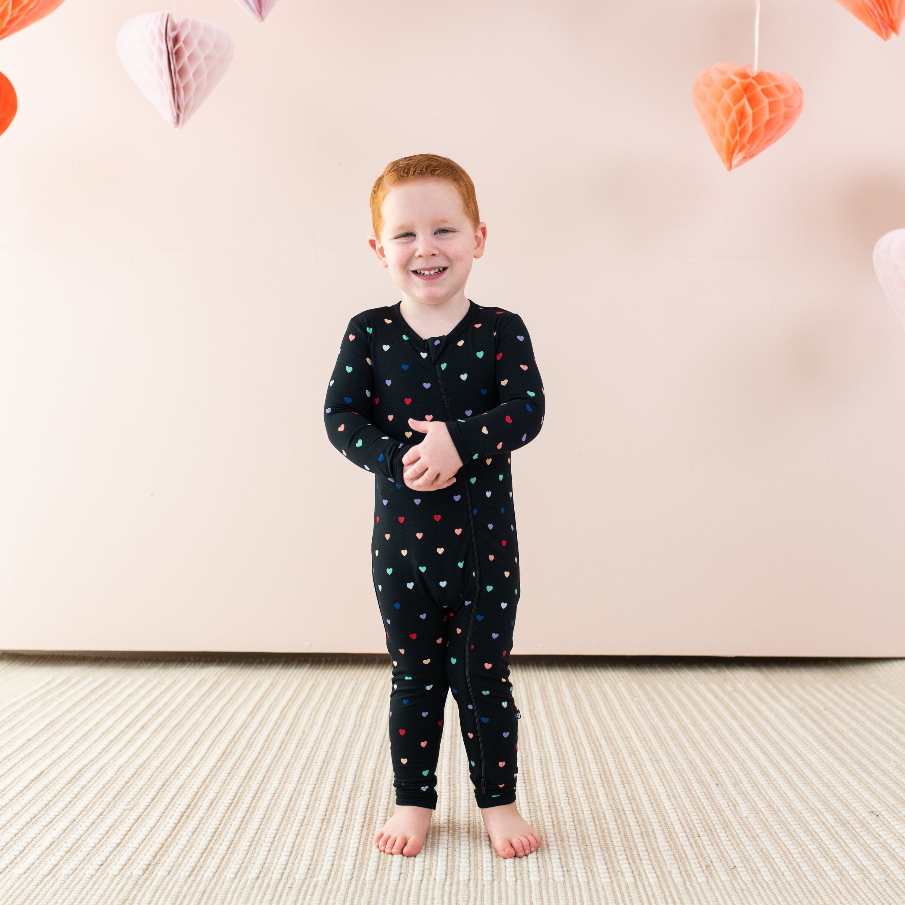 Toddler wearing Kyte Baby Zippered Romper in Midnight Rainbow Heart