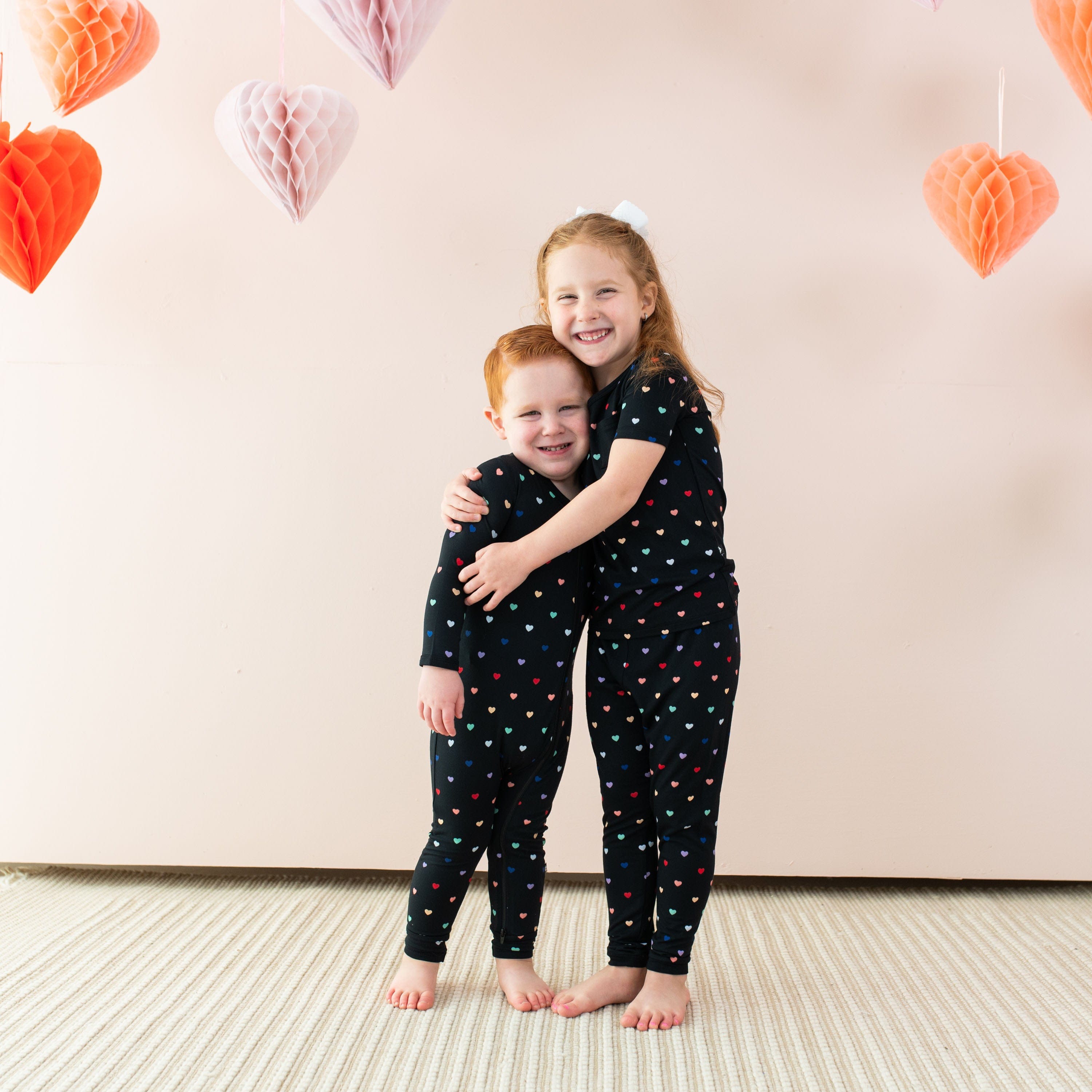 Siblings wearing Kyte Baby matching pajamas in Midnight Rainbow Heart