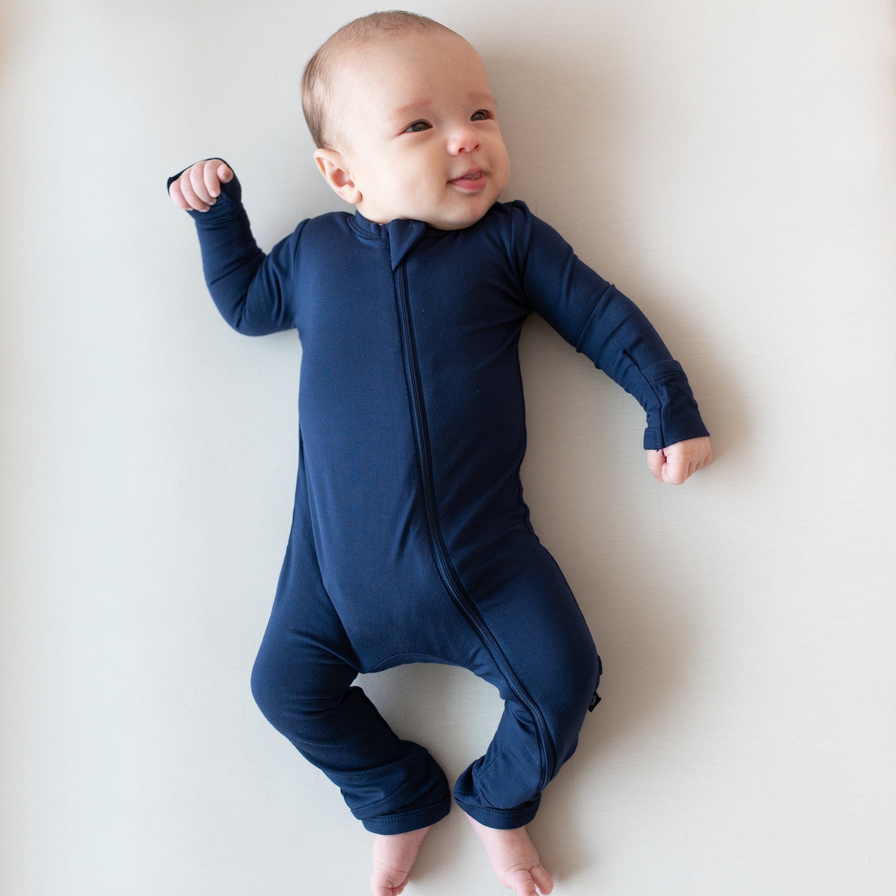 Infant laying on an Oat surface while wearing a Zippered Romper in Navy